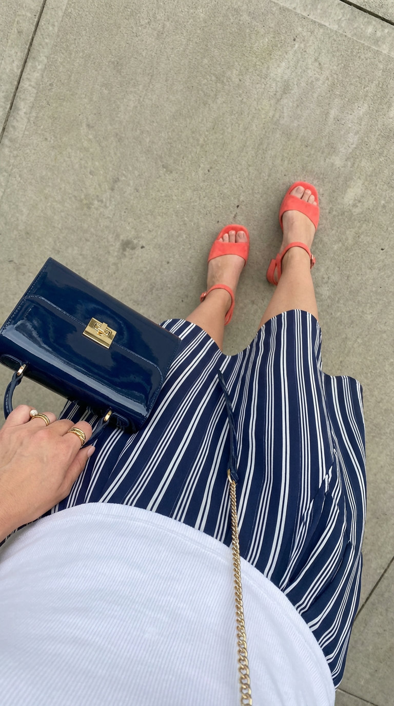Chic Preppy Summer Outfits for Evening 2024 Chic preppy summer outfit featuring a navy and white striped midi skirt, white ribbed top, coral sandals, and a navy patent mini bag for a sophisticated evening.