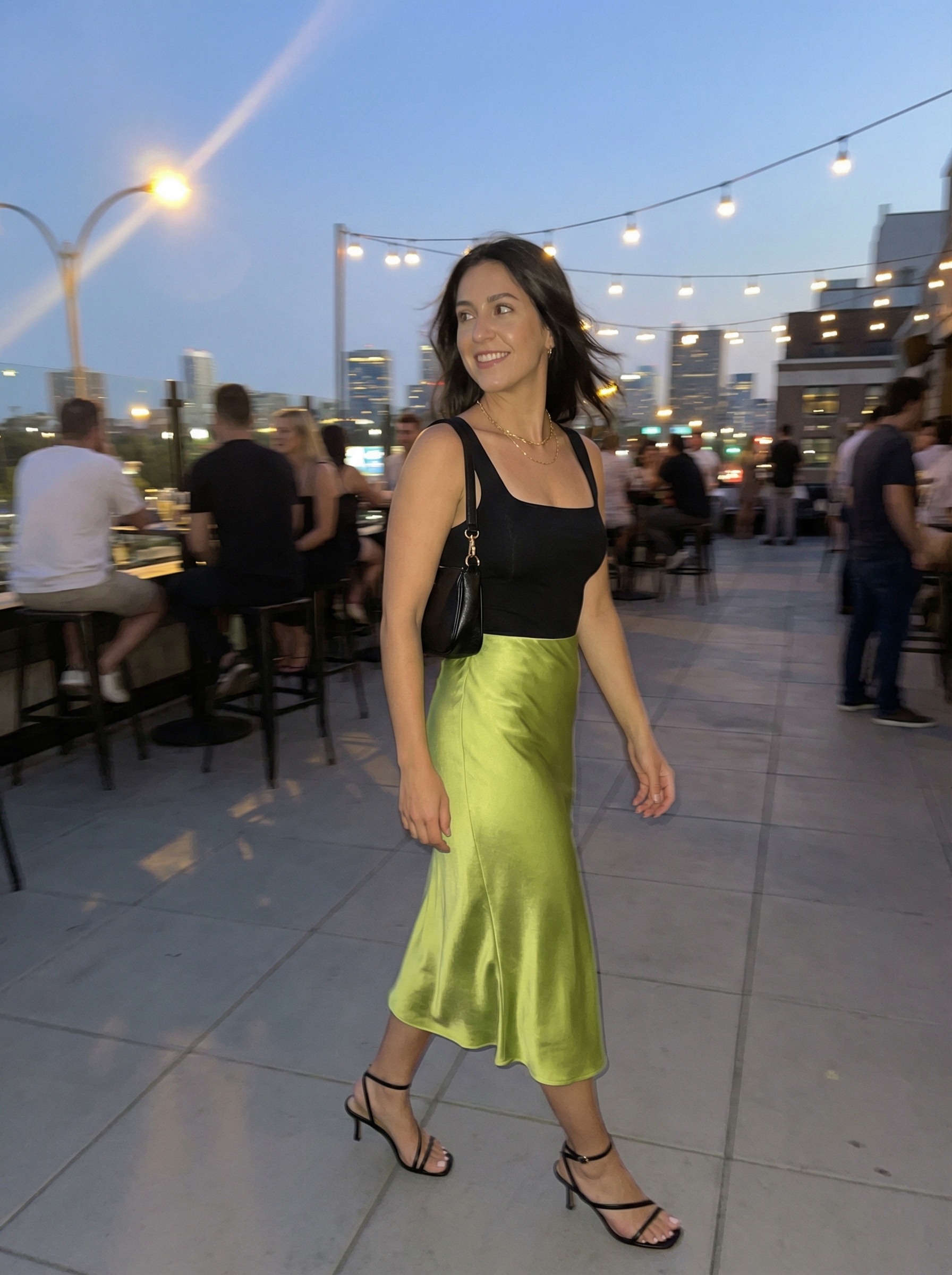 A sultury lime green satin bias-cut slip midi skirt paired with a fitted black square neck tank top for colorful summer outfits 2026, accessorized with minimalist black strappy heels and delicate gold necklaces.