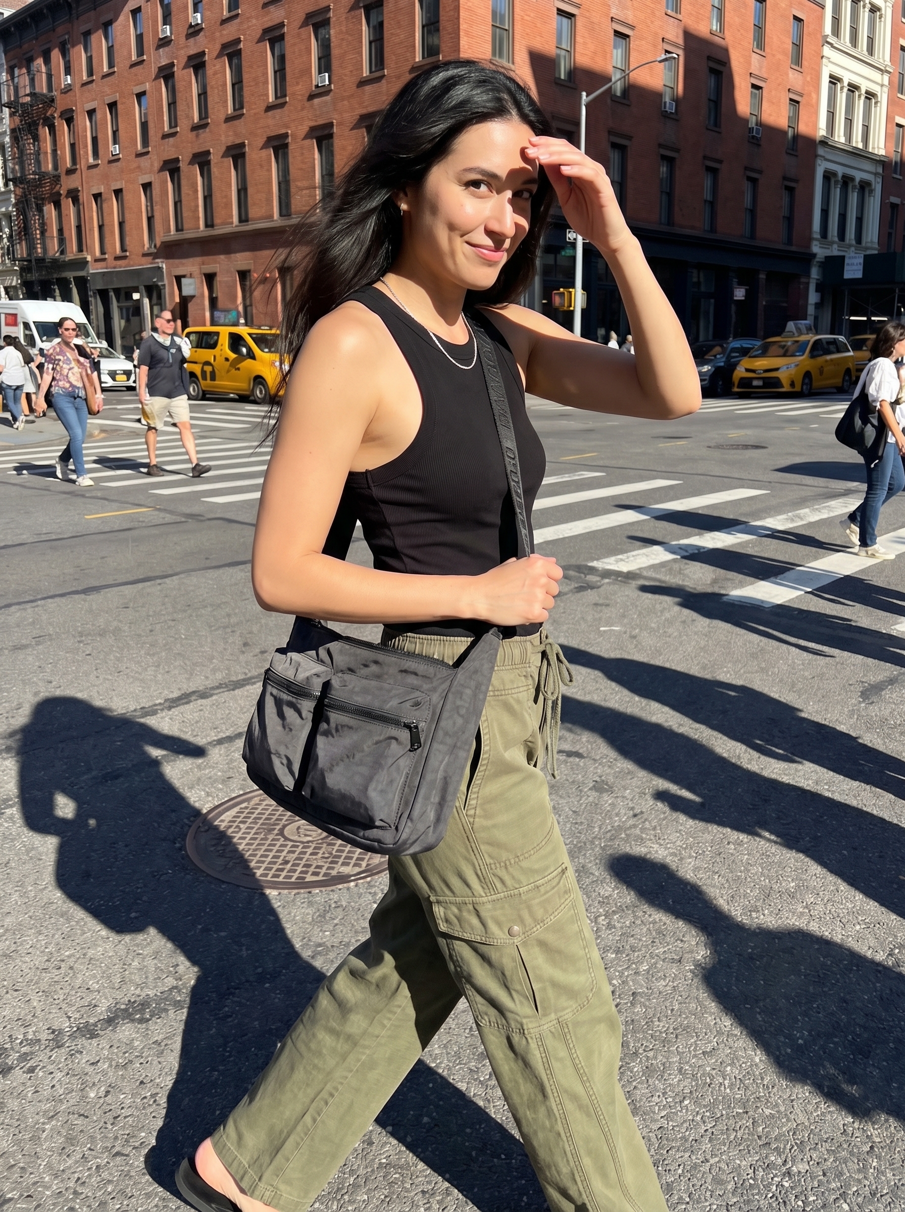 An adventurous cool summer outfit with olive green cargo pants, a black racerback tank top, white low-top sneakers, and a utility crossbody bag for city sightseeing.