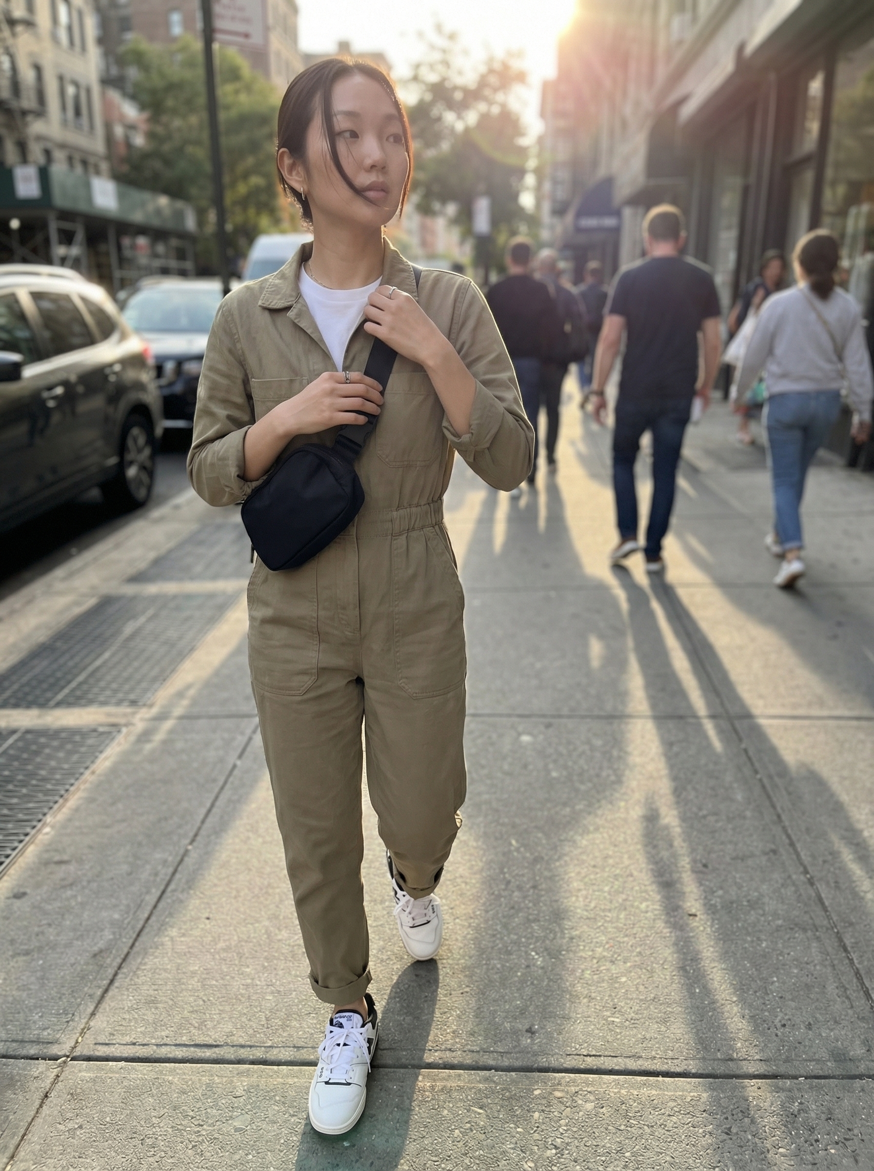 Urban Explorer Summer Jumpsuit 2024 An urban explorer rocks a khaki utility jumpsuit layered over a white t-shirt, chunky sneakers, and a black belt bag, making it a cute comfy outfit for summer shopping or day trips.