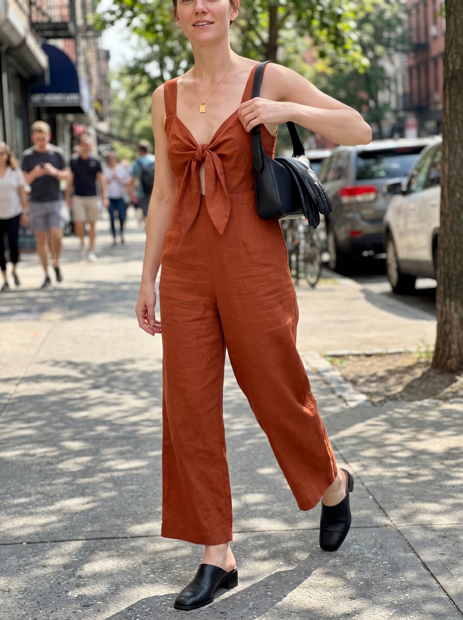 Chic terracotta wide-leg jumpsuit with black flat mules, a gold geometric necklace, and a black mini bag, a sophisticated option for cute outfits for summer 2026.