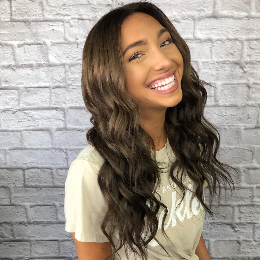 Beautiful woman with long, dark, wavy hair styled with subtle auburn highlights, perfect for dark summer hair ideas 2026, posing outdoors.