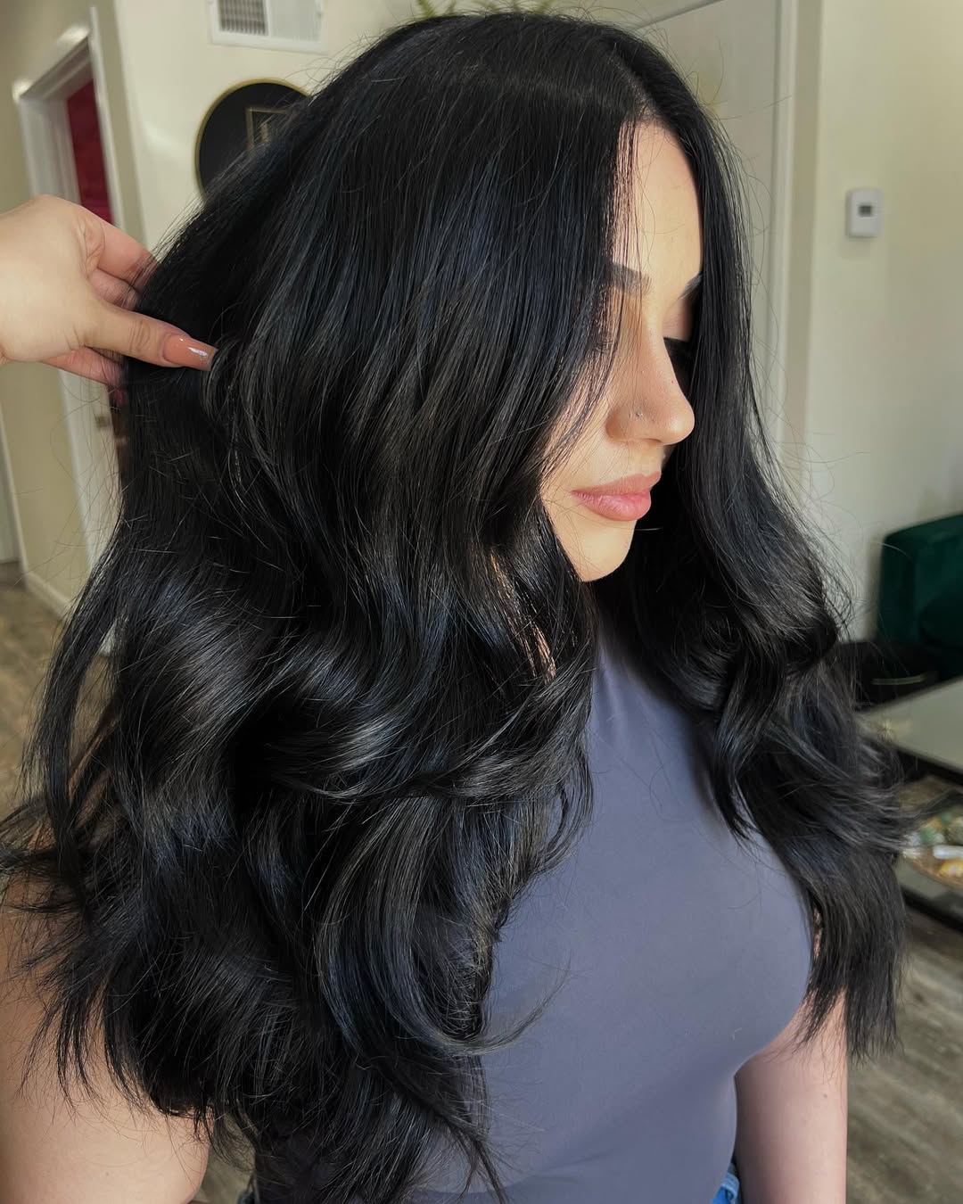 Close-up of a woman with dark wavy hair, featuring subtle caramel highlights, ideal for dark summer hair ideas 2026. Her hair flows naturally over her shoulders, framing a radiant, sun-kissed face.