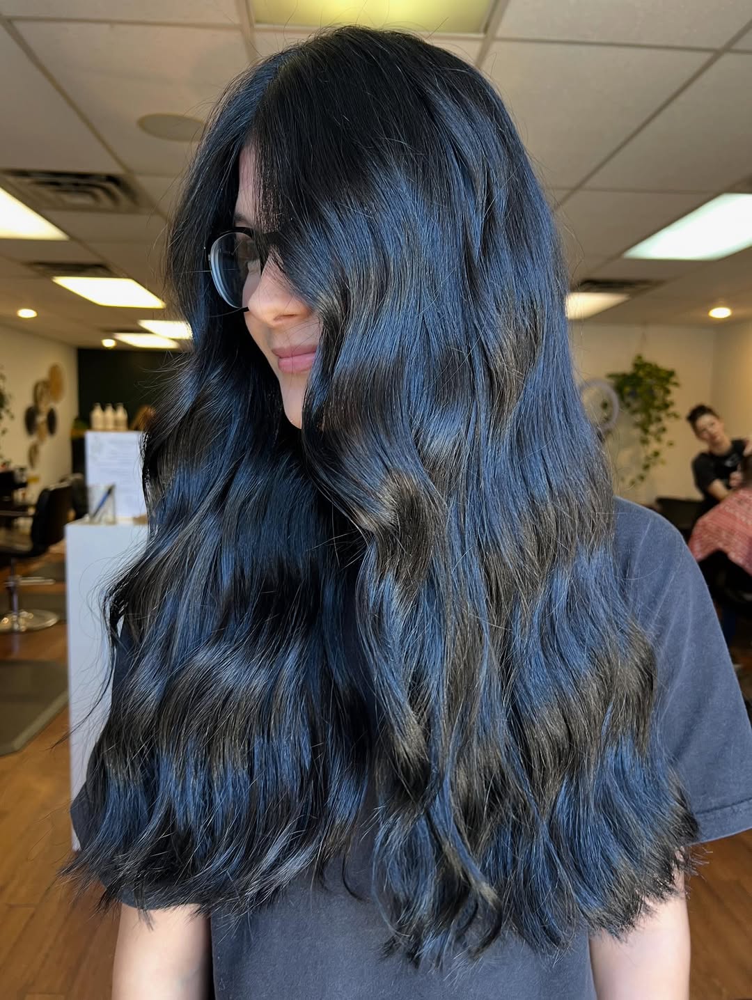 Beautiful woman with long, dark wavy hair styled in soft curls against a vibrant summer backdrop, showcasing dark summer hair ideas. Her hair shines under the sun, perfect for a casual outdoor look.