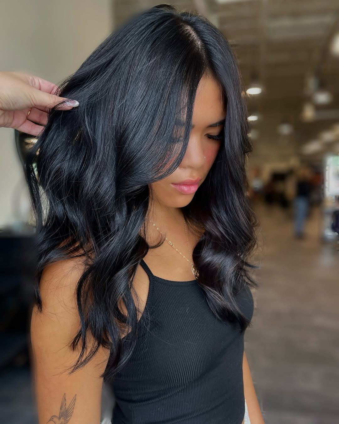 A woman with long, shiny dark brown hair styled in soft waves, showcasing a beautiful dark summer hair idea. She wears a flowy white sundress, perfect for a beach vacation.