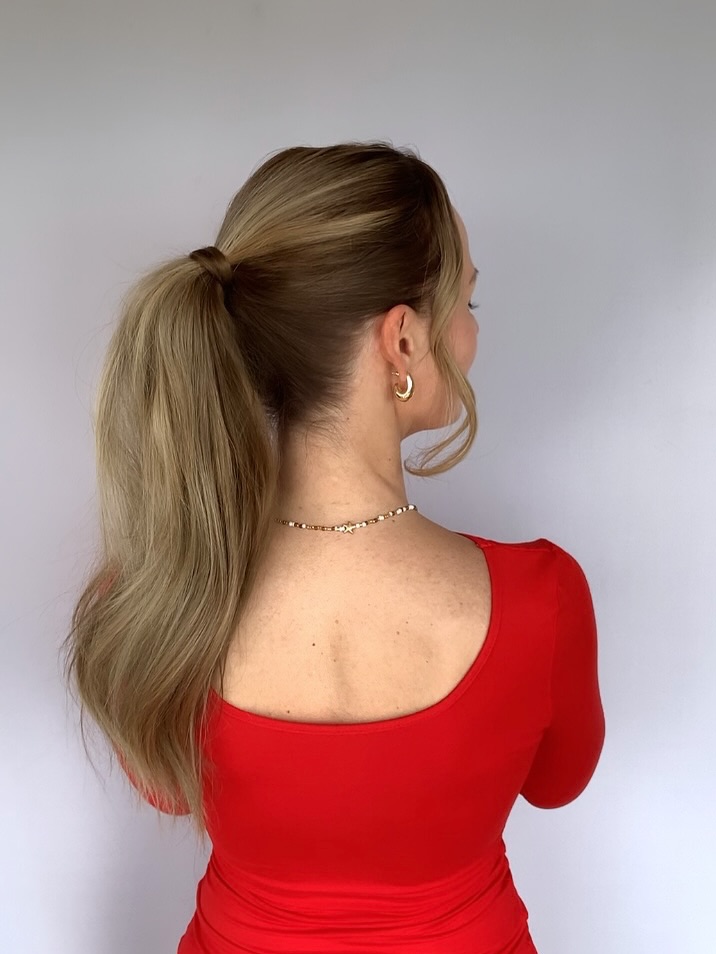 A woman with radiant red hair showcasing a half-up braided ponytail, a perfect easy summer hairstyle for 2026. This casual look is ideal for beach days or outdoor events.