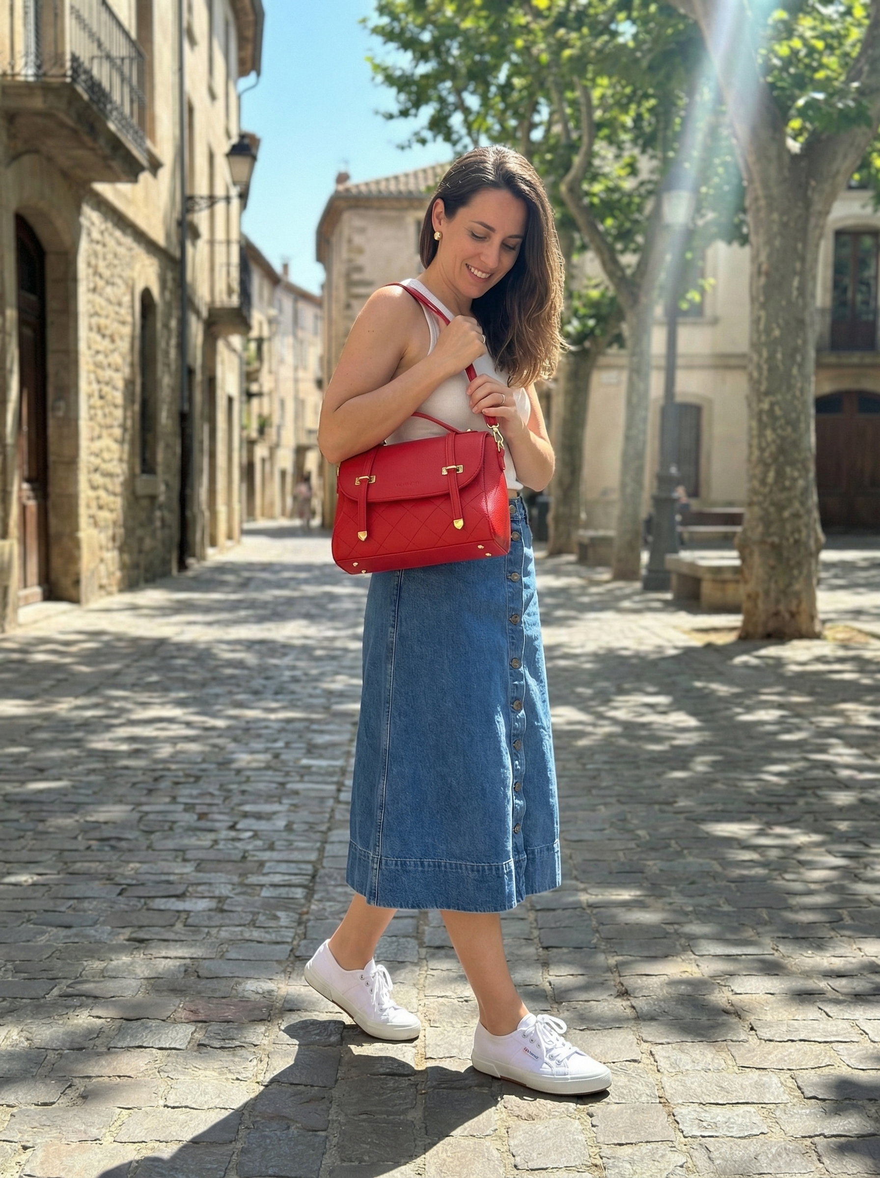 Chic late summer outfit featuring a navy and white striped top, denim midi skirt, red crossbody bag, and white sneakers for a classic coastal look.