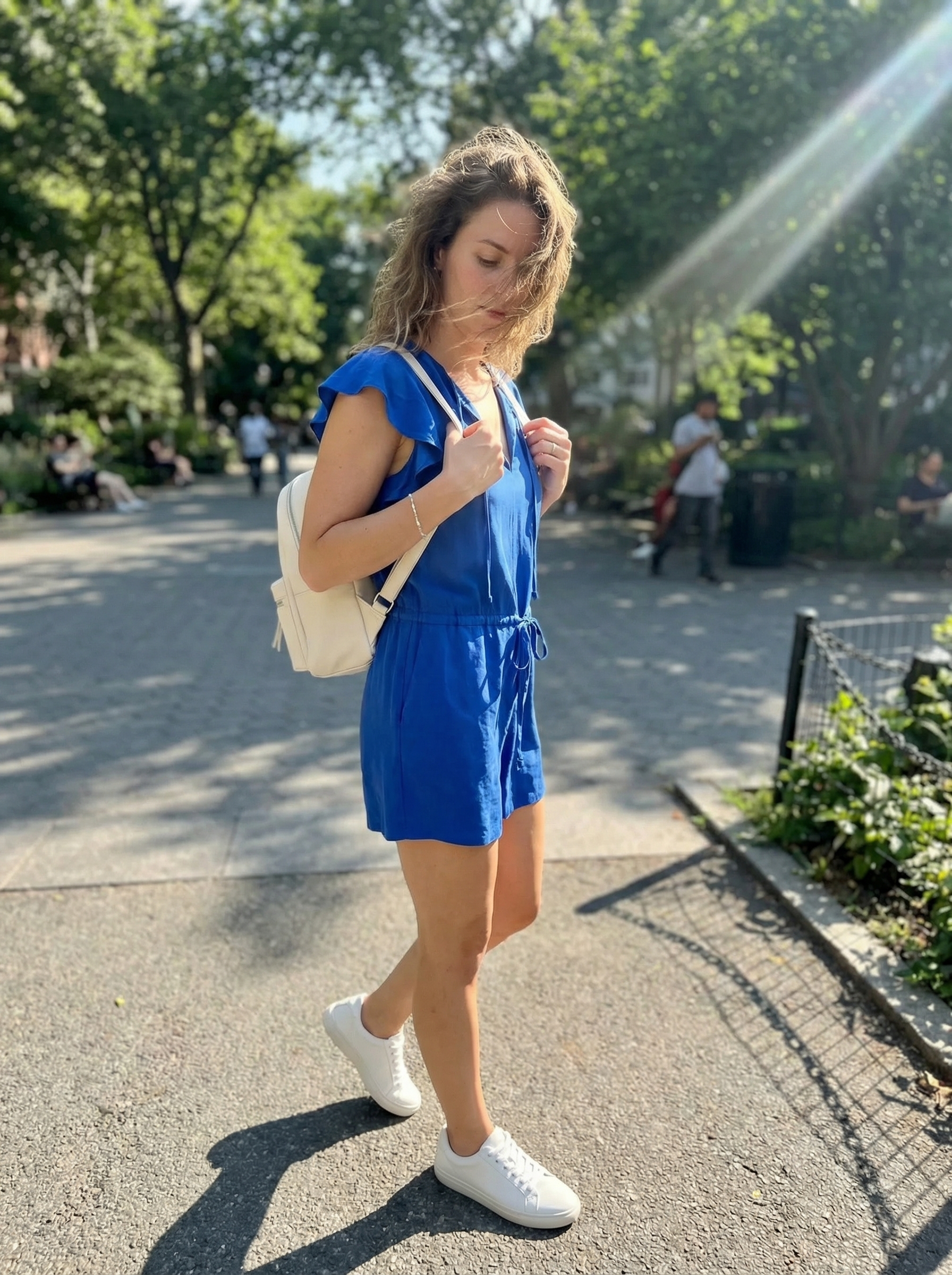Playful cobalt blue tailored romper with a drawstring waist, styled with clean white low-top sneakers and a white mini backpack, a youthful option for late summer outfits.