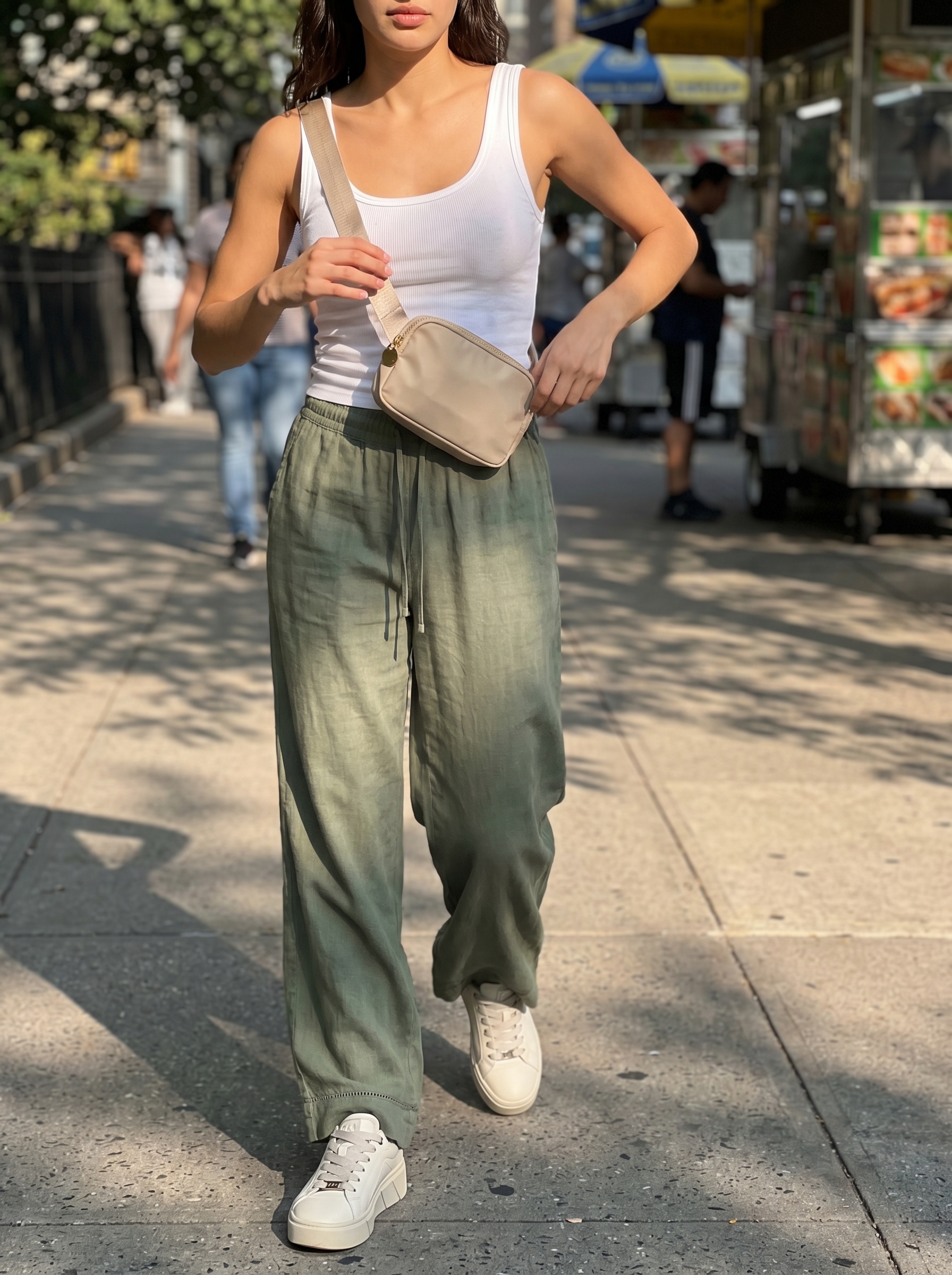 City sightseeing outfit featuring light olive wide-leg linen pants, a white fitted tank, and off-white platform sneakers, perfect for a light summer color palette 2026. Accessorized with a cream belt bag.