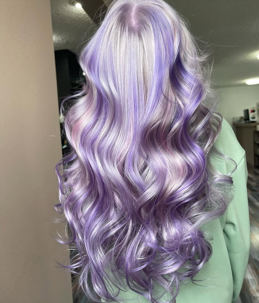 A woman with a beautiful soft summer hair color 2026, featuring golden blonde highlights, styled in loose waves, wearing a light blue denim jacket.