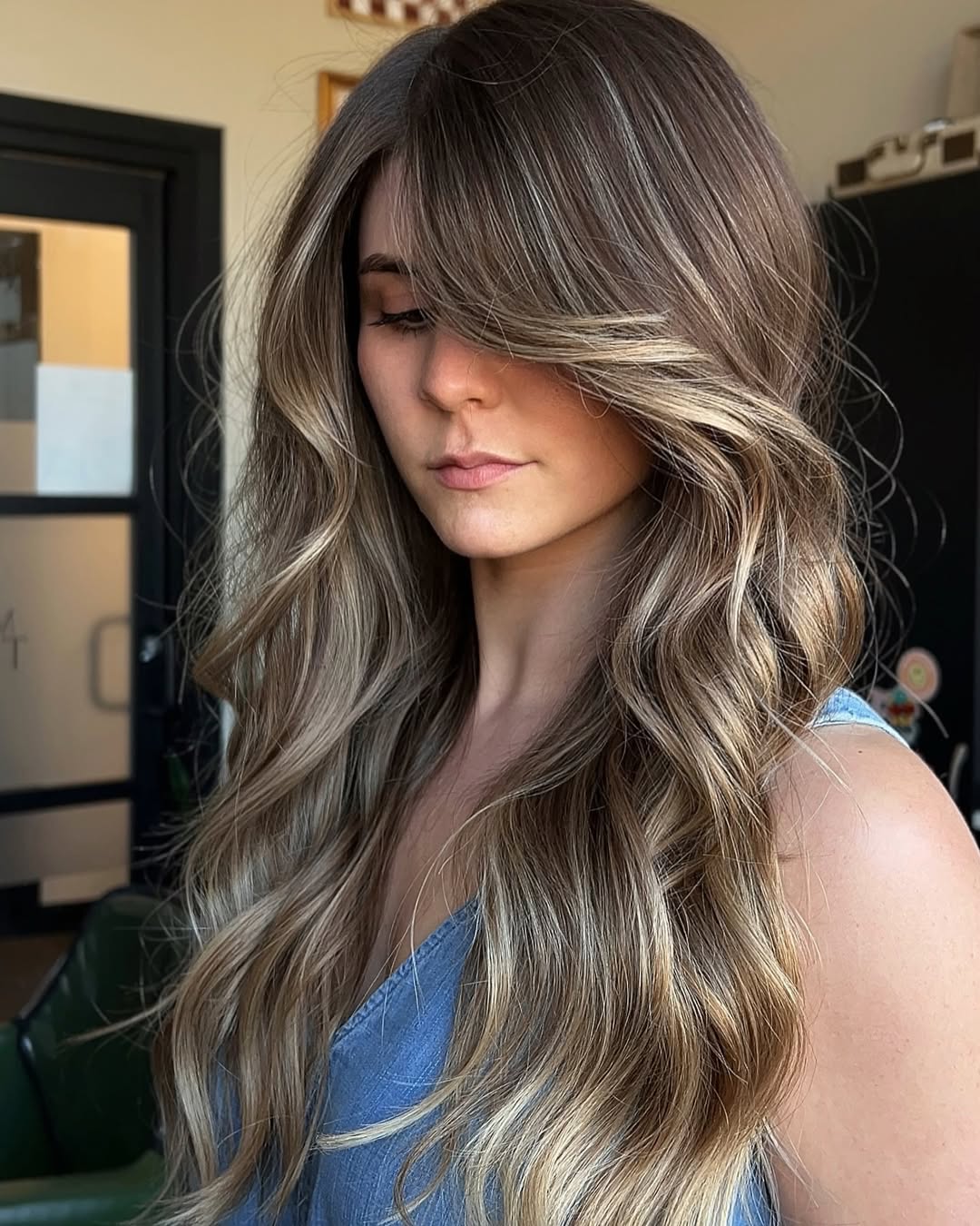 A woman with perfectly styled mousy brown hair, showcasing a beautiful soft summer hair color 2026, paired with a light blue top for a casual daytime look.