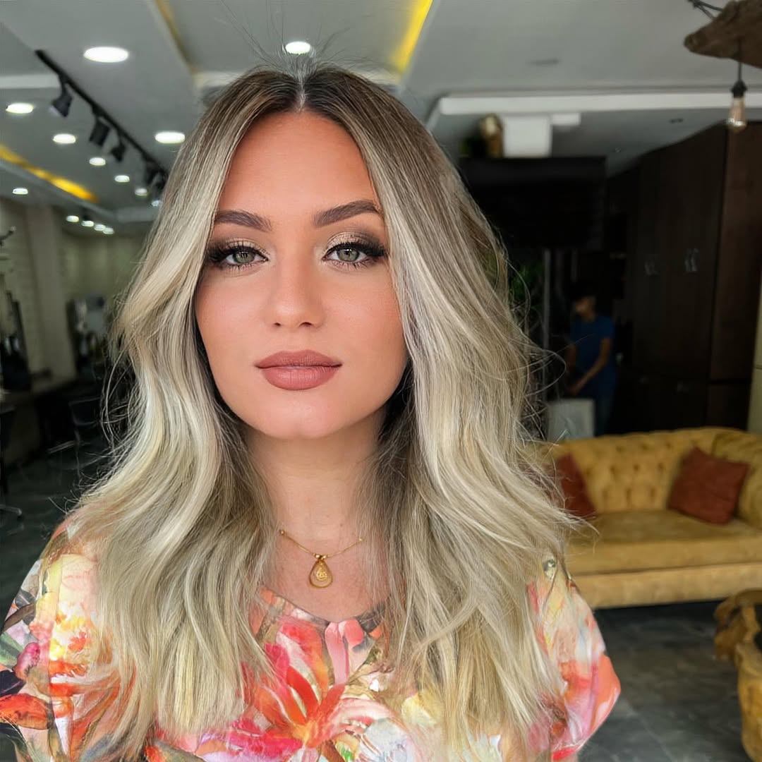 Young woman with soft summer hair color 2026, featuring subtle highlights, posing in a pastel pink satin slip dress for a romantic evening event.