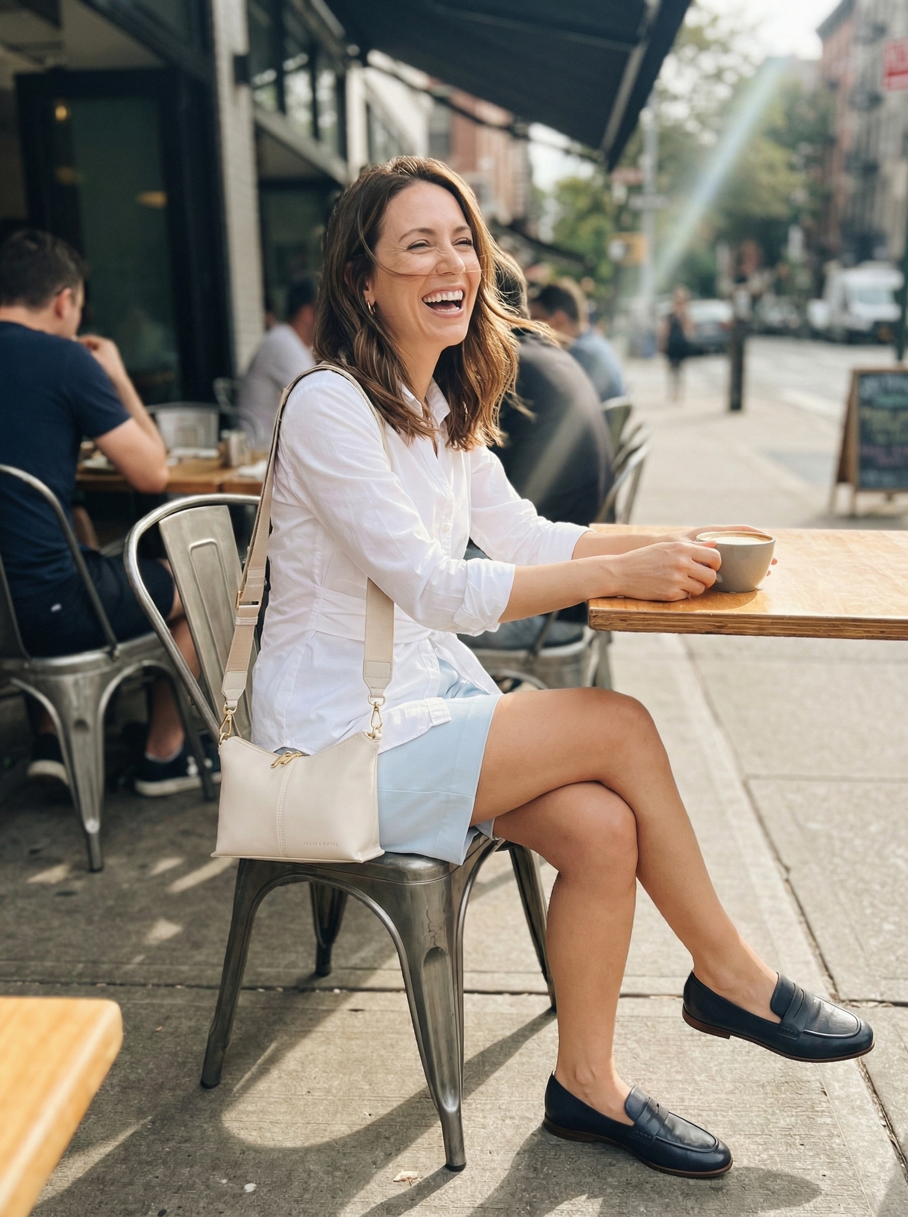 Fresh preppy spring summer outfits with light blue tailored Bermuda shorts, a white tied button-down shirt, navy leather loafers, and a white structured crossbody bag for a picnic.