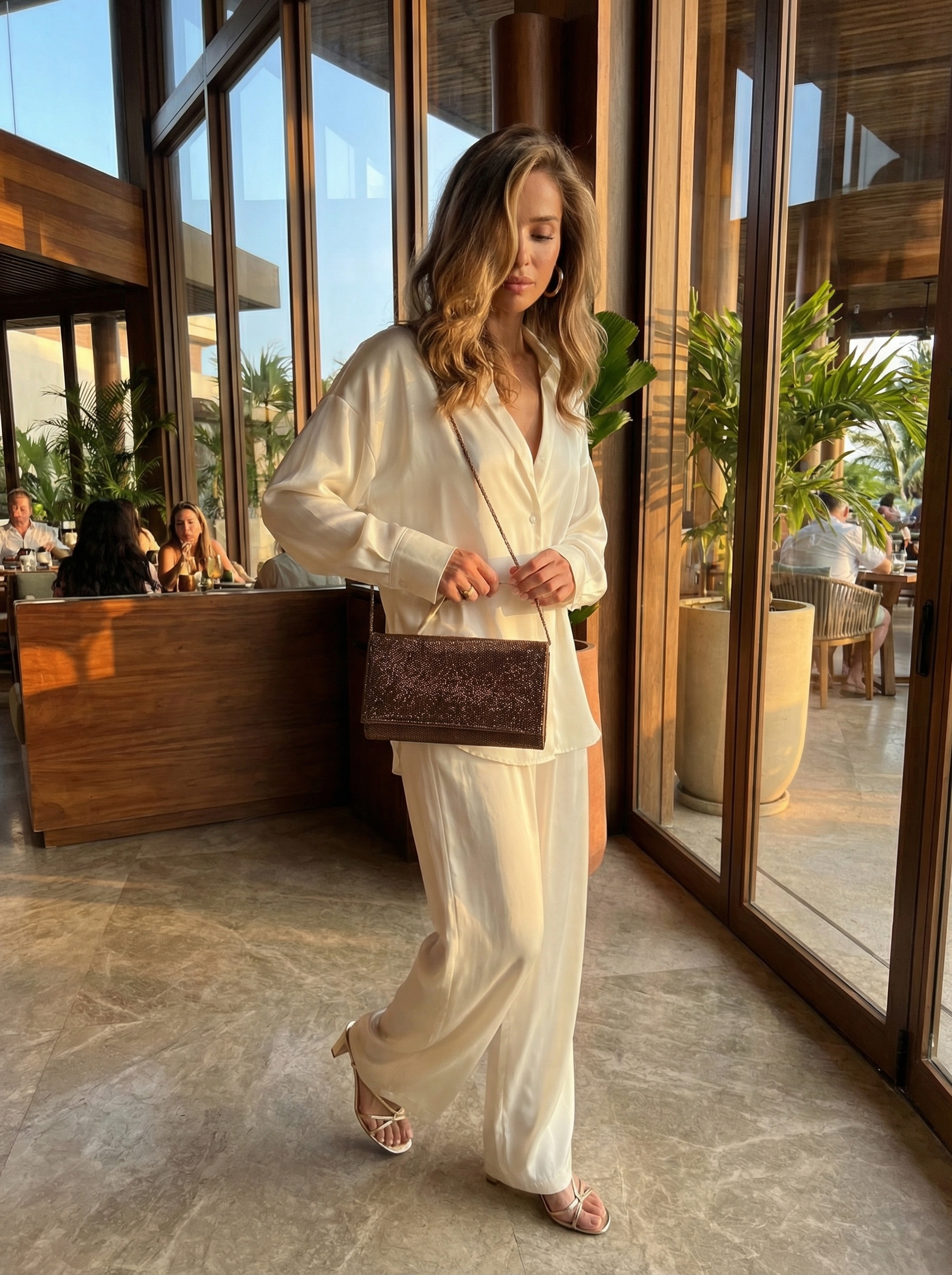 Glamorous ivory satin matching set for spring summer outfits, featuring wide-leg pants, a sleeveless top, gold metallic sandals, and a bronze clutch, perfect for a resort dinner or vacation evening.