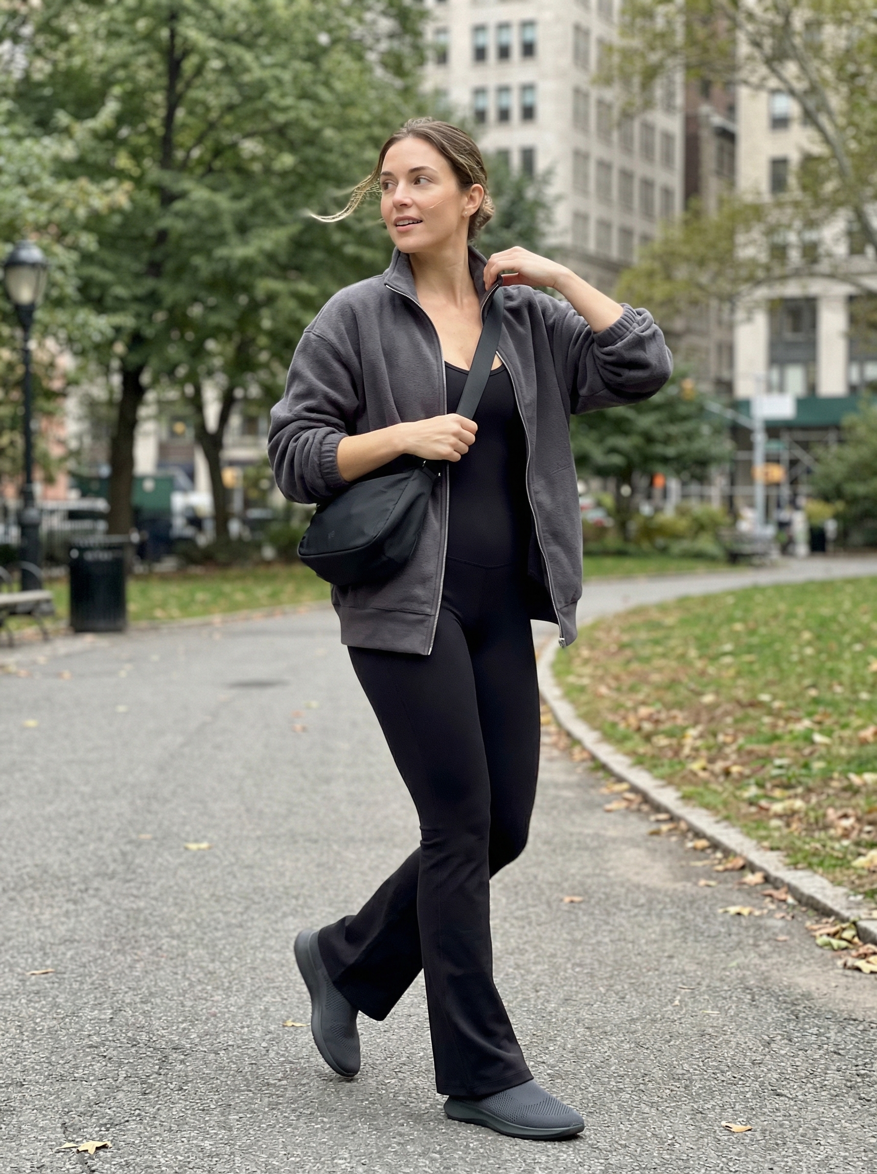 Sleek monochrome charcoal grey unitard jumpsuit with a black zip-up hoodie and athletic sneakers, offering a modern summer athleisure outfit 2026.