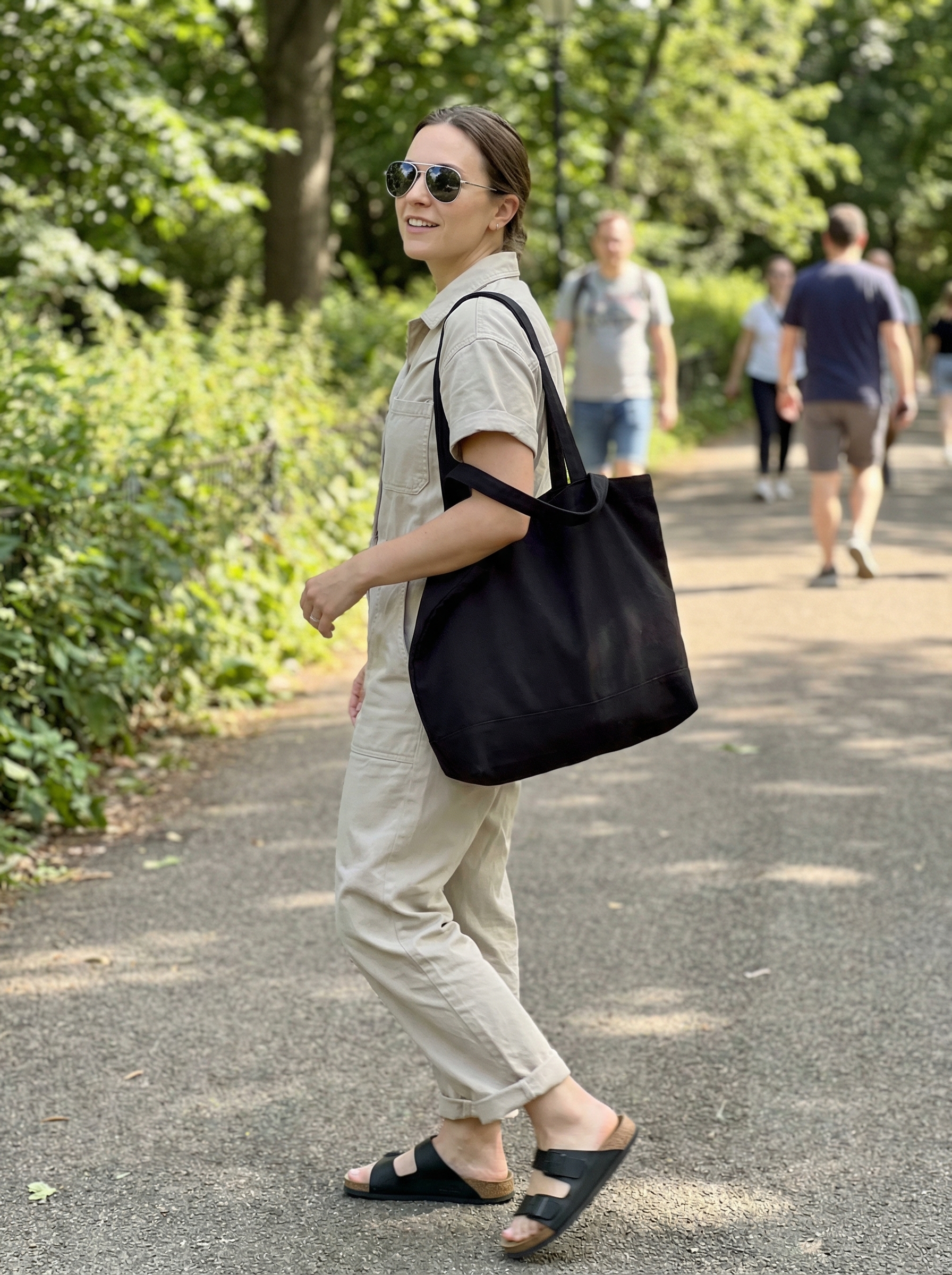A practical summer athleisure outfit 2026 with a stone beige utility jumpsuit, black slide sandals, and a canvas tote, ideal for a weekend getaway.
