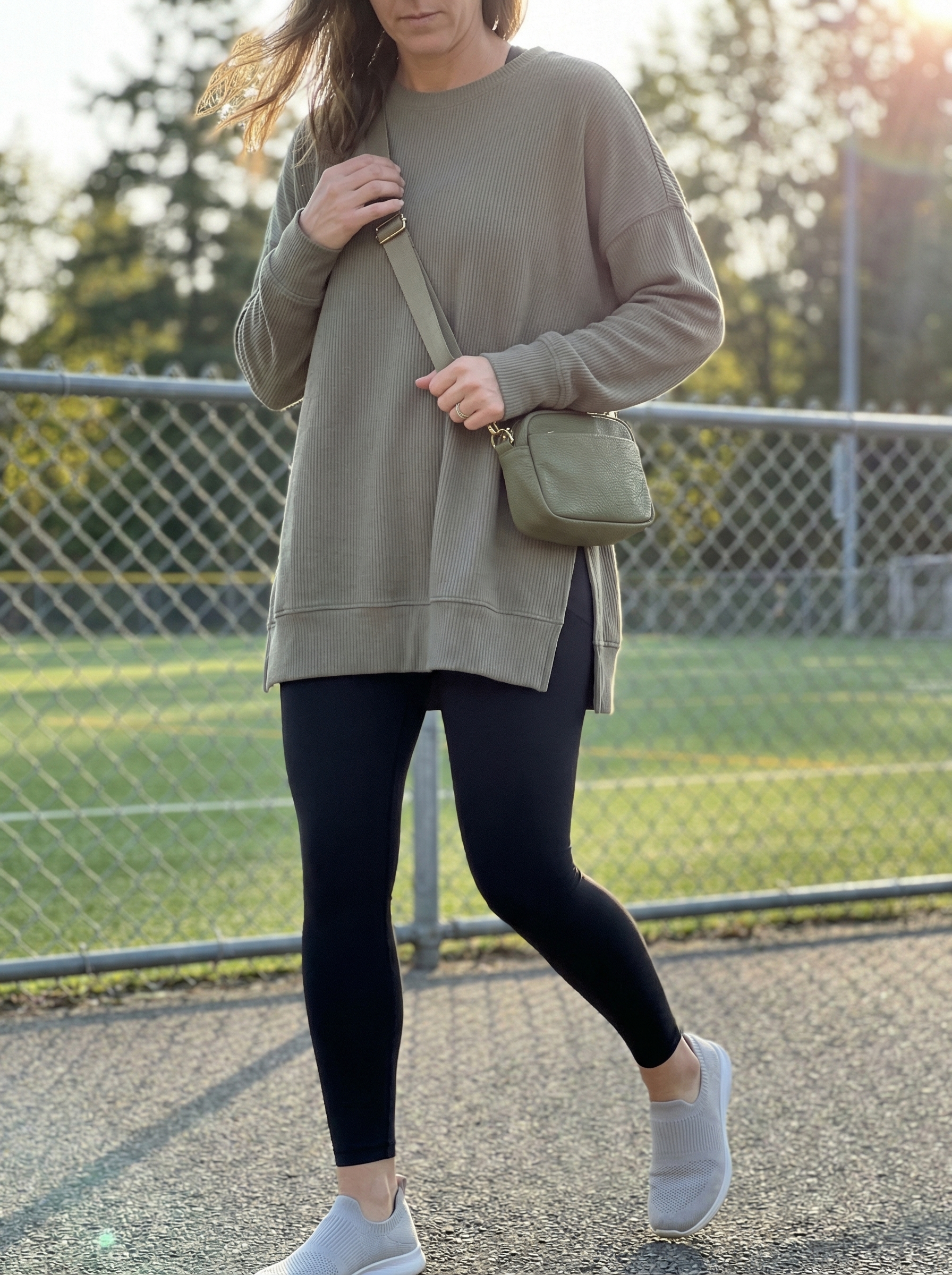 Cozy olive green oversized tunic top with black leggings and cream slip-on sneakers for a relaxed weekend summer athleisure outfit 2026.