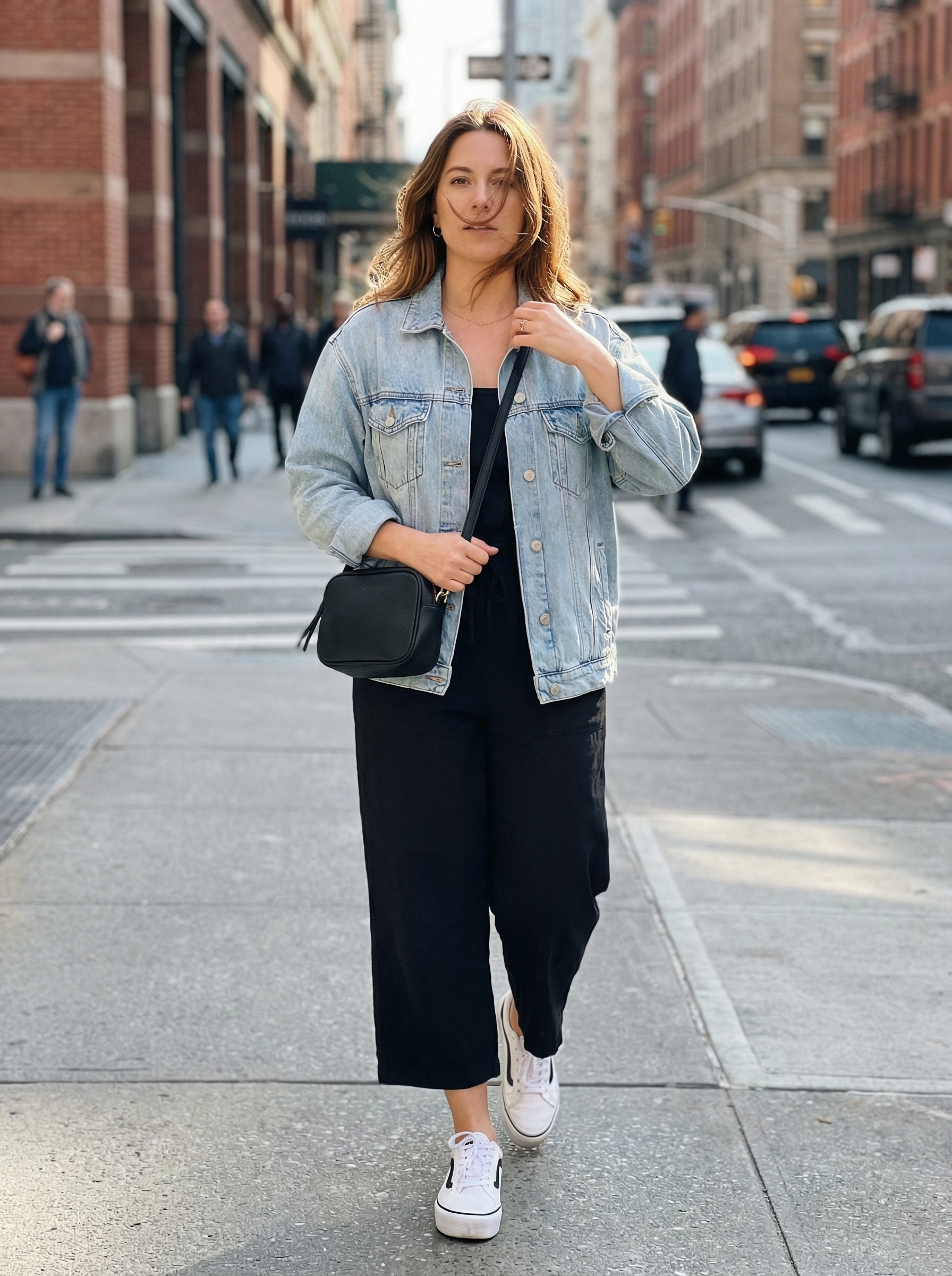A modern black and light wash denim summer athleisure outfit for women, showcasing a Tencel jumpsuit, an oversized denim jacket, and white platform sneakers, perfect for brunch.