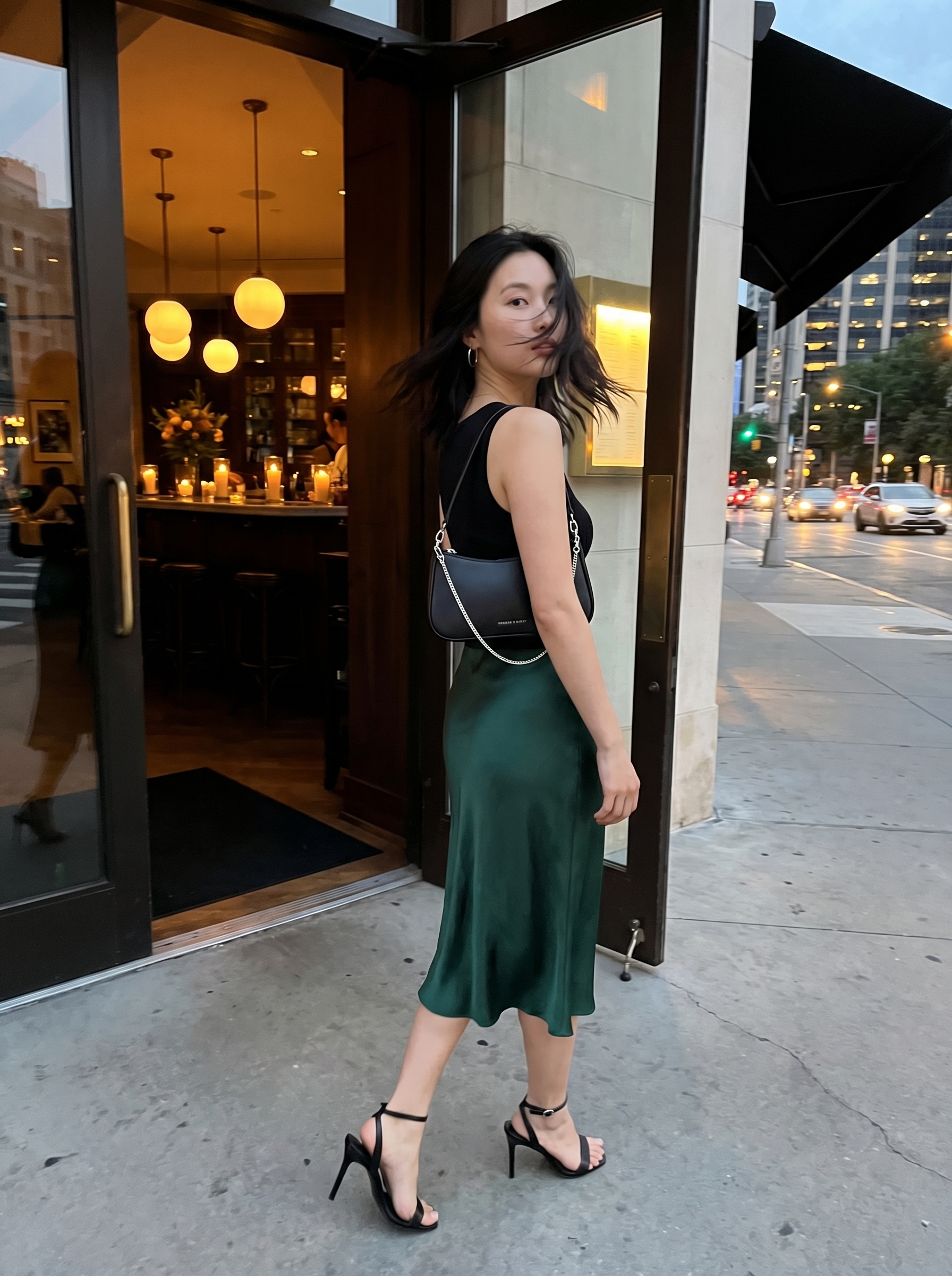 Chic summer bar outfit 2026 with an emerald green satin midi skirt, black ribbed knit top, and minimalist strappy heels. Ideal for cocktail bars and date nights.