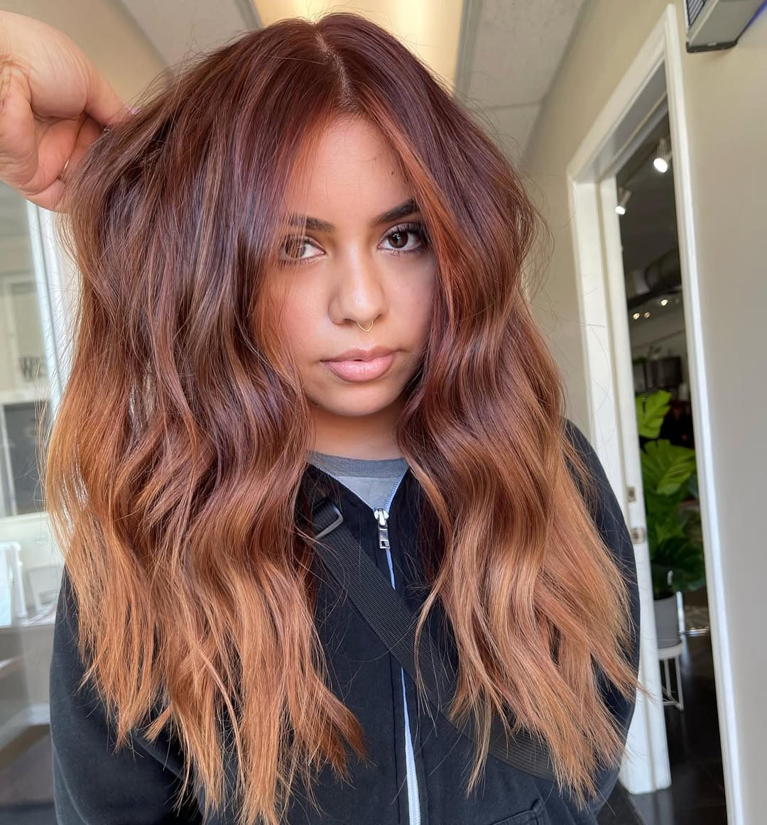 Close-up of a woman with vibrant red, curly hair styled in a chic half-updo, perfect for summer hair ideas 2026. The style features face-framing curls and a playful top knot.