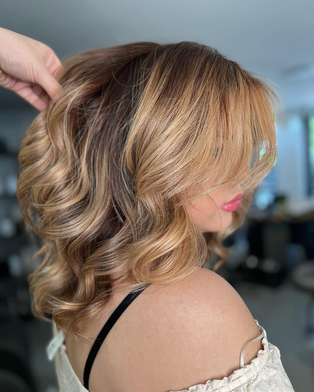 Woman with long, wavy blonde hair styled in a half-up, half-down look with a delicate braid, perfect for summer hair ideas 2026. She wears a flowy white dress in a sunny outdoor setting.