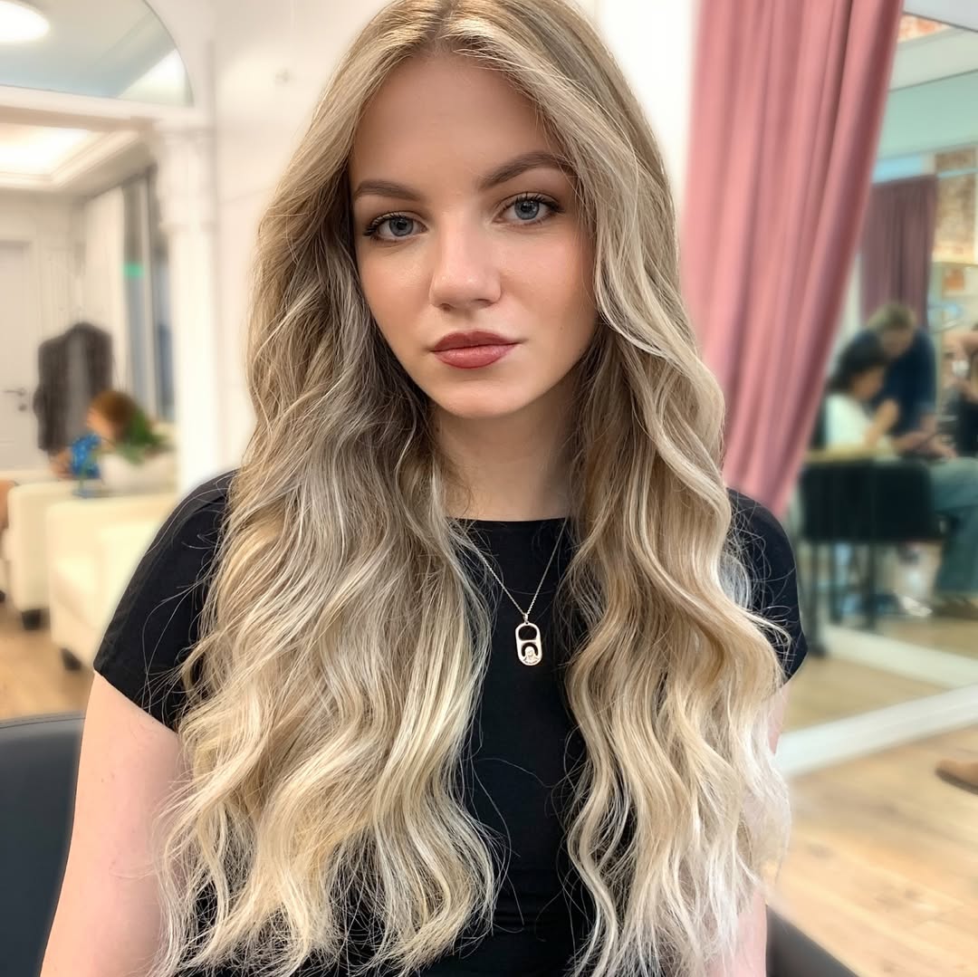 A woman with long, shiny dark hair styled in voluminous loose waves, showcasing a beautiful summer hairstyle for long hair.