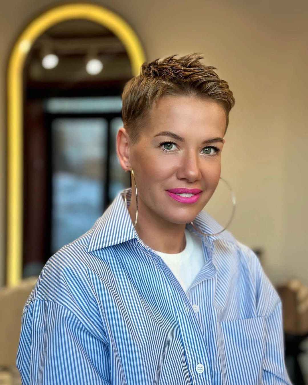 Blonde woman with short, wavy hair styled in a chic, voluminous side part, showcasing a trendy summer hairstyle for short hair 2026. She wears a flowy white dress.