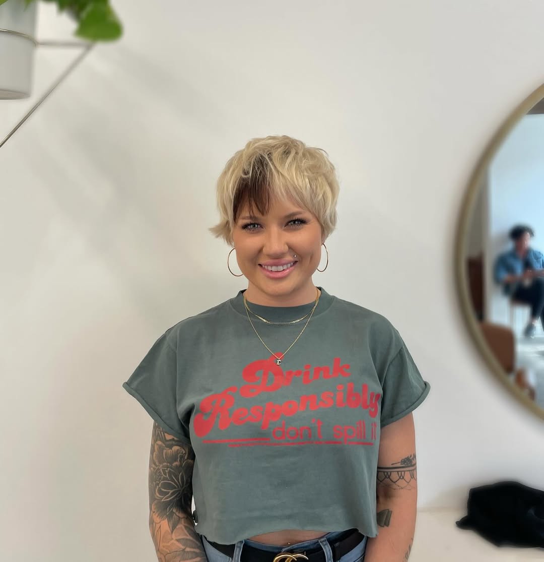 A woman confidently poses outdoors, her short, wavy bob styled with subtle highlights, perfect for summer hairstyles for short hair. She wears a relaxed, light-colored blouse, ideal for a casual daytime look.