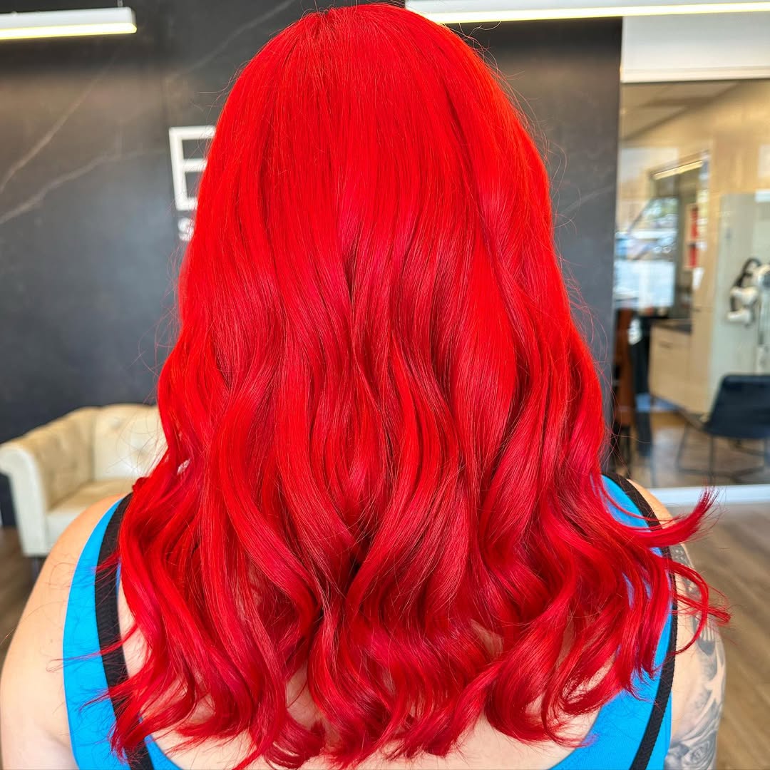 Woman with vibrant summer red hair color 2026 styled in soft waves, wearing a chic white linen crop top and high-waisted denim shorts, perfect for a casual sunny day out.
