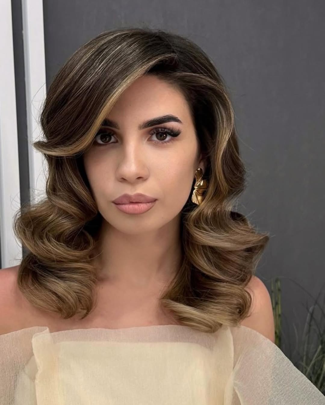 Elegant brunette woman with a sleek, low chignon bun with delicate face-framing tendrils, perfect for a summer wedding guest hair 2026.