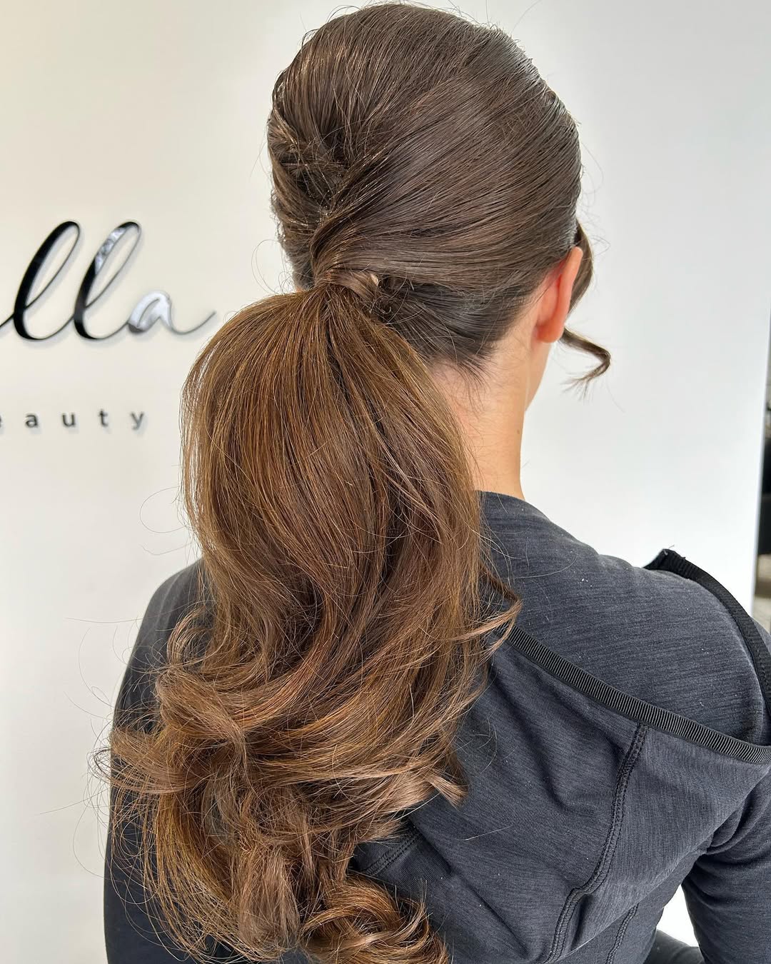 Elegant brunette woman with a chic updo, perfect for summer wedding guest hair 2026. Her hairstyle features soft waves pulled back, framing her face beautifully, ideal for a formal outdoor celebration.