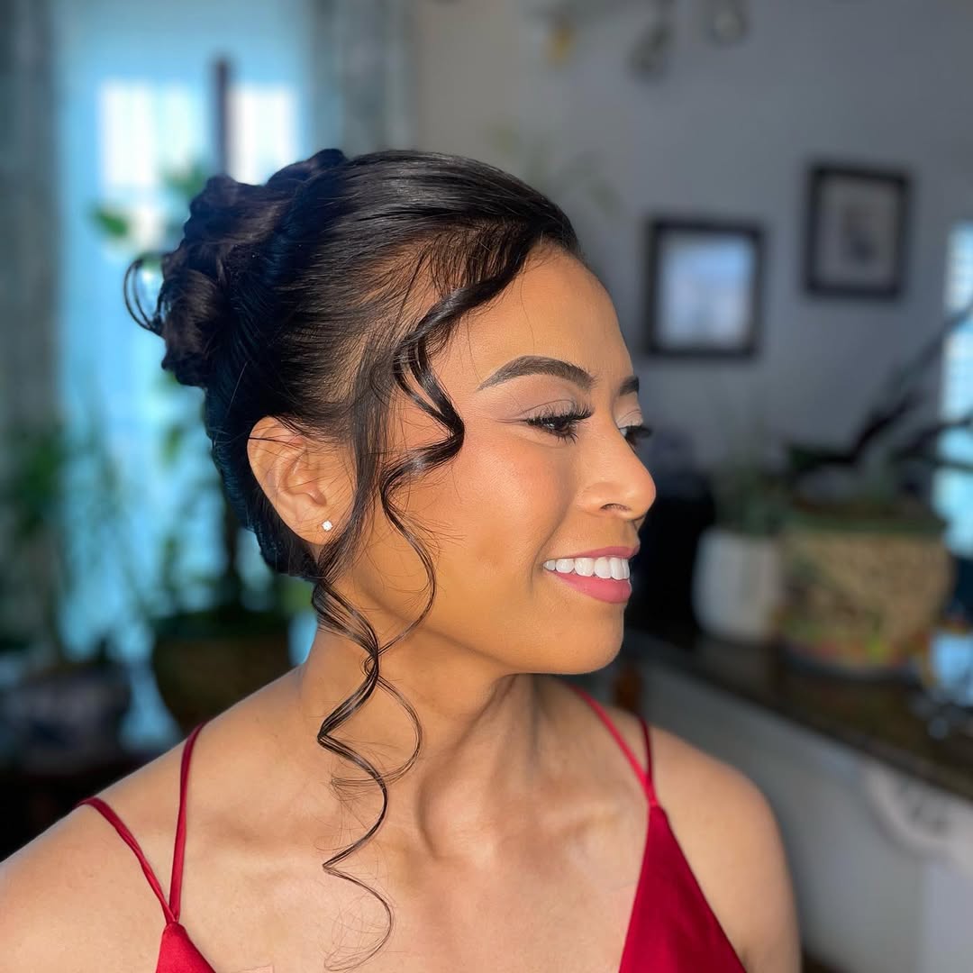 Elegant brunette bride with her hair styled in a chic low bun with wispy face-framing tendrils, perfect for a summer wedding guest hair 2026. She wears a white floral dress with delicate straps.