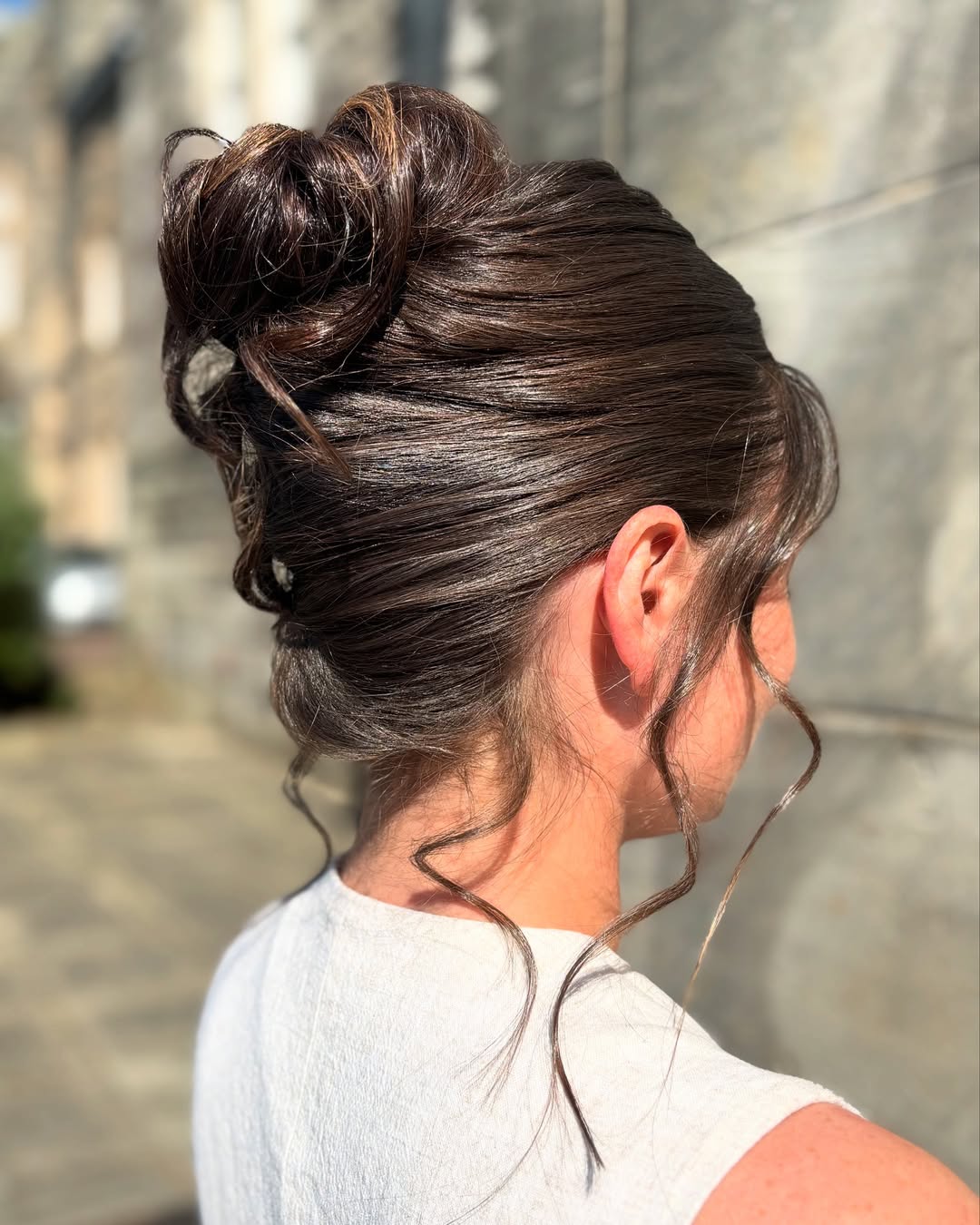 Elegant brunette woman with a loose, softly curled updo, perfect for summer wedding guest hair 2026. Her hair is styled with subtle face-framing pieces and a refined finish.