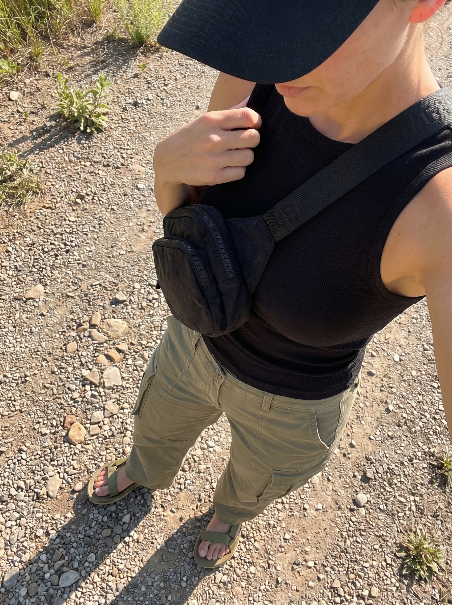 Adventurous western summer outfit 2026: khaki green cargo pants, a black racerback tank, a black baseball cap, and olive green hiking sandals for outdoor exploration.