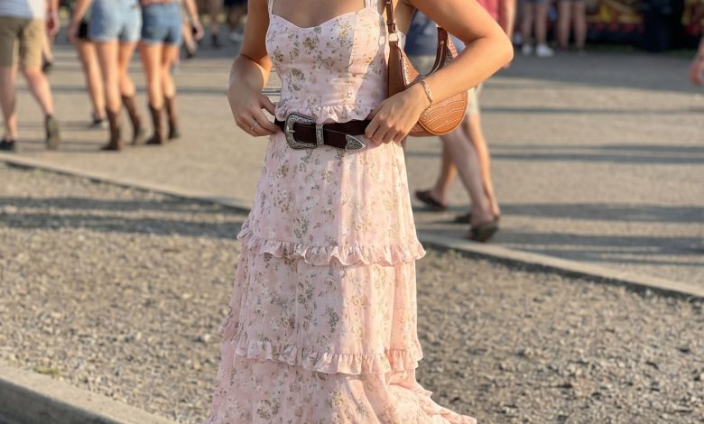 Feminine western summer outfit 2026: a dusty rose floral maxi dress, classic cowboy boots, a structured saddle bag, and a wide western belt for an outdoor concert.