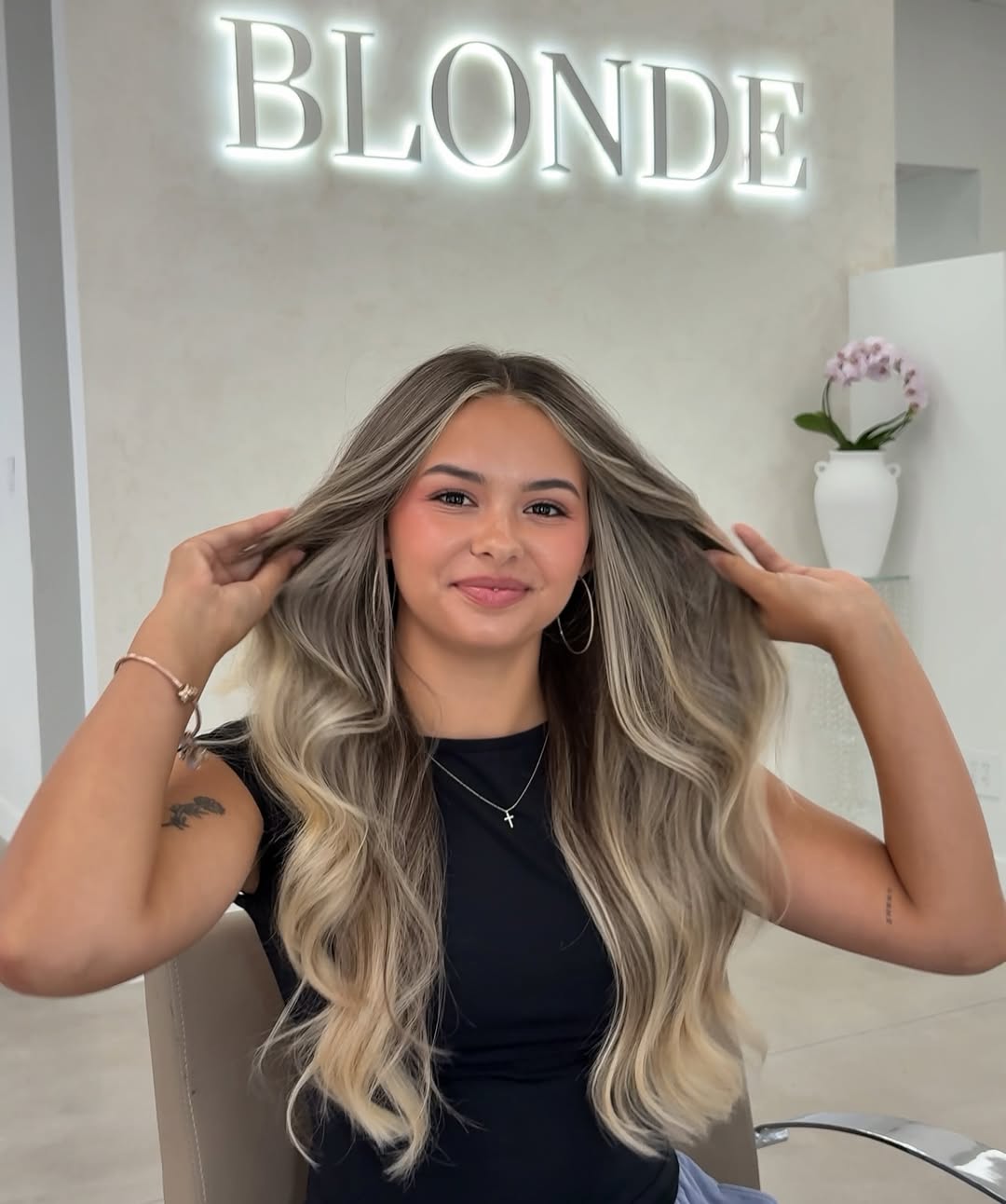 Blonde hair inspo summer 2026 for a woman with sun-kissed, wavy blonde hair styled in a half-updo with face-framing layers, perfect for a casual sunny day outfit.