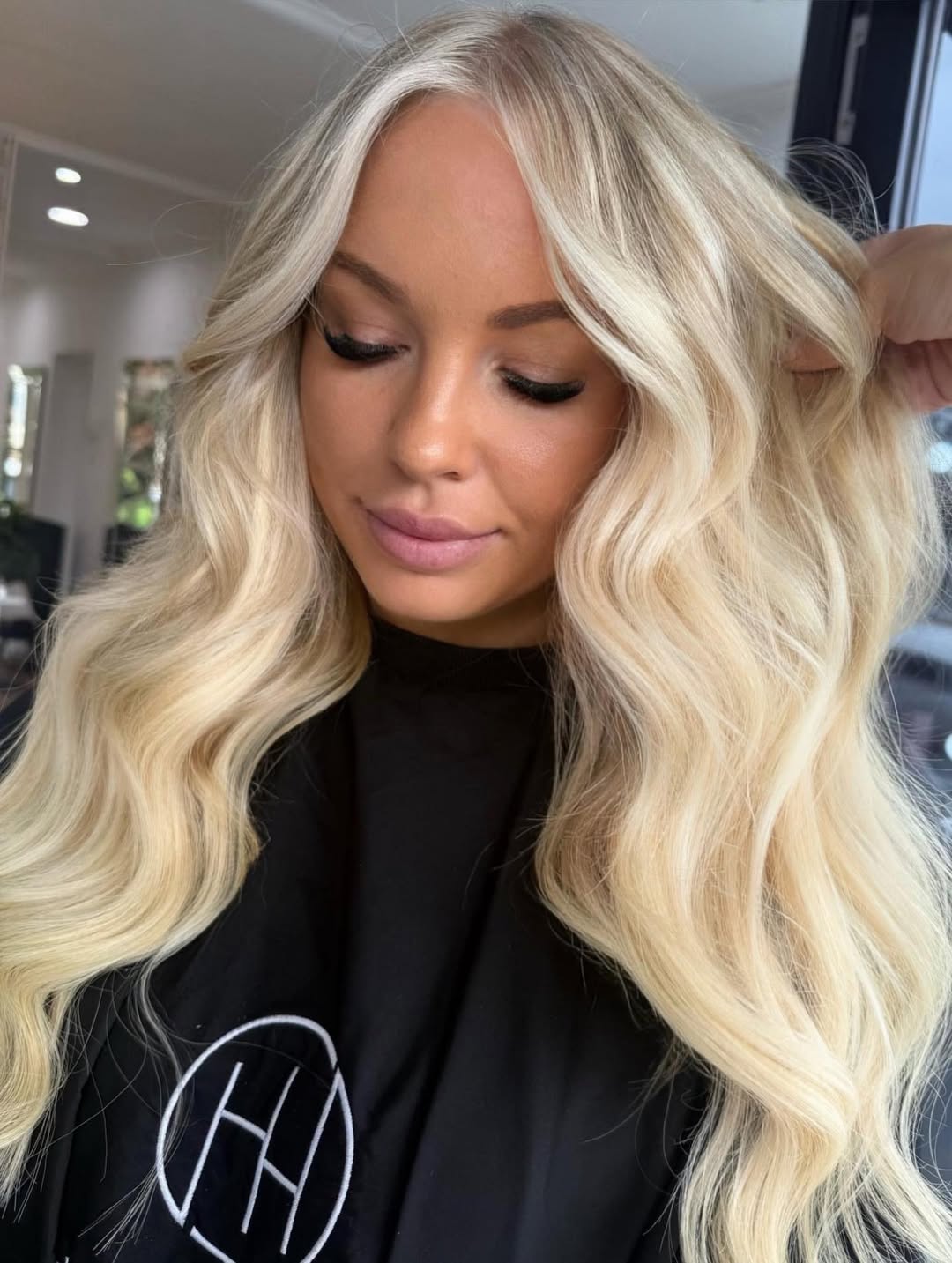 A woman with radiant blonde hair inspo summer 2026, styled in soft waves, wearing a chic white linen dress, perfect for a sunny outdoor brunch.