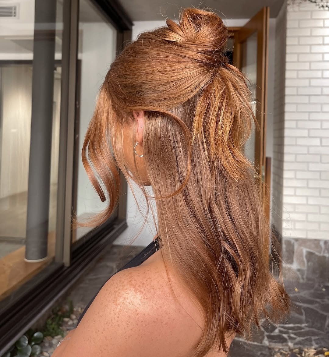 Close-up of a woman with long, sun-kissed brown hair styled in soft, beachy waves, perfect for cute summer hair ideas. Her hair is parted down the middle, frames her face beautifully, and has subtle highlights, suggesting a relaxed, effortlessly chic look for warm weather.