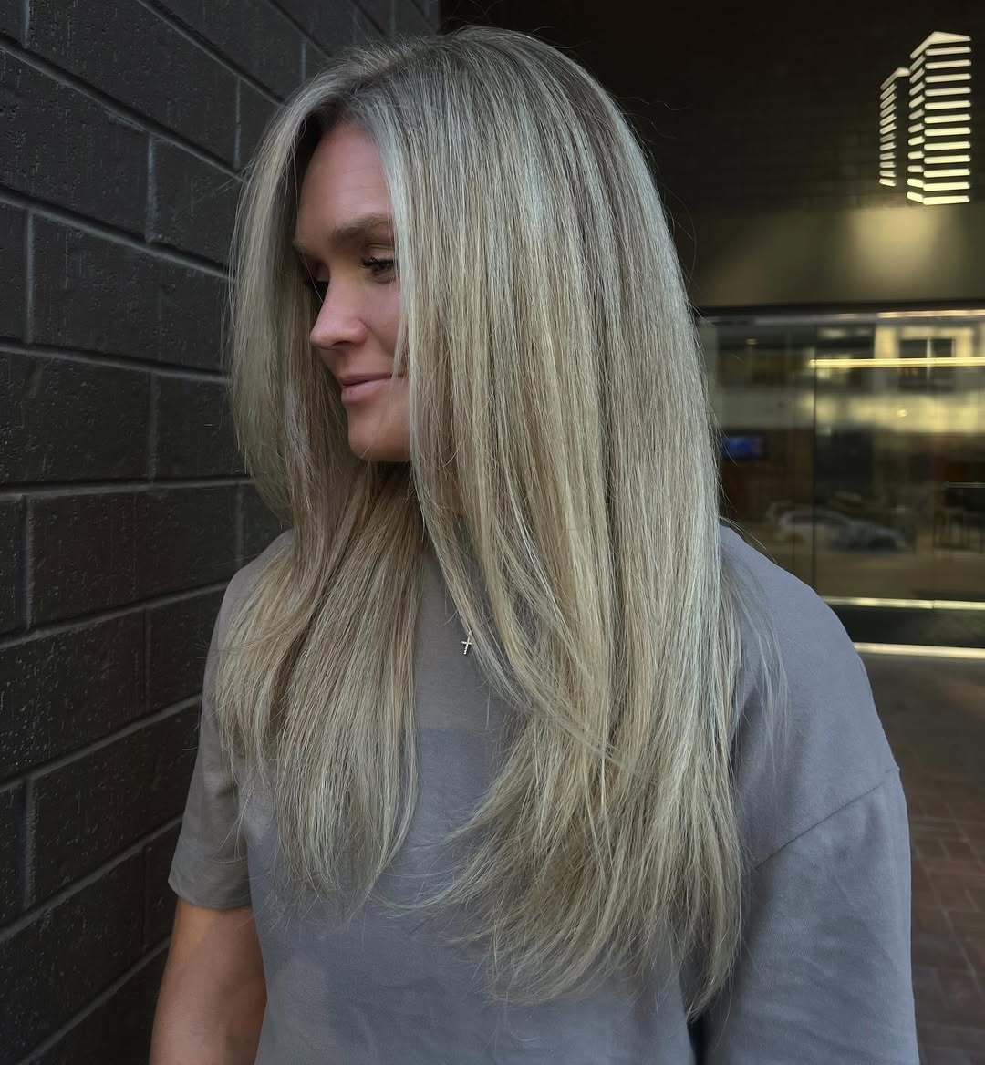 Close-up of a woman with vibrant soft summer blonde hair styled in loose waves, showcasing a natural, sun-kissed look against a light background.