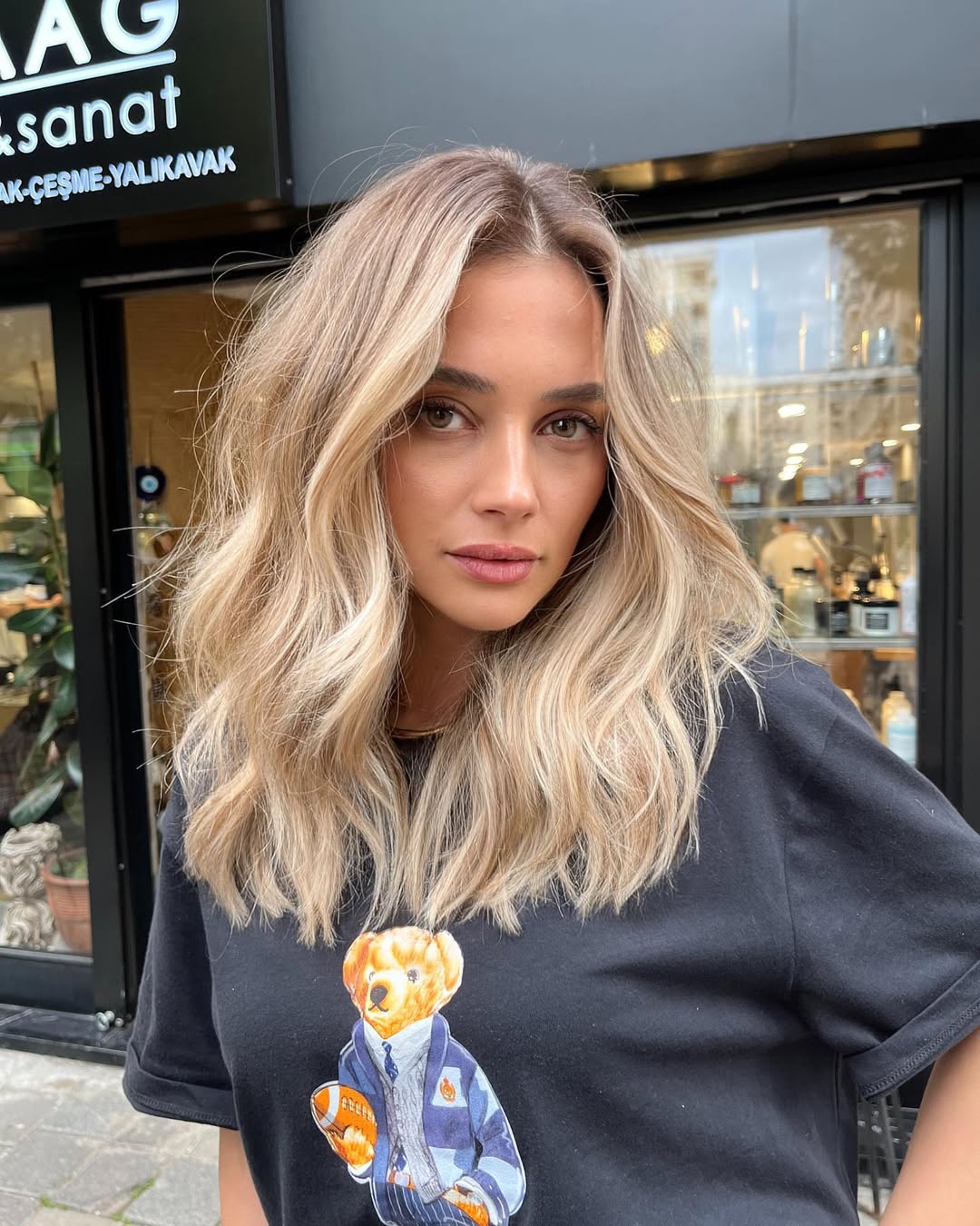 Close-up of a woman with radiant soft summer blonde hair styled in loose waves, paired with a delicate pearl necklace. Her natural makeup enhances her warm skin tone for a chic, everyday look.