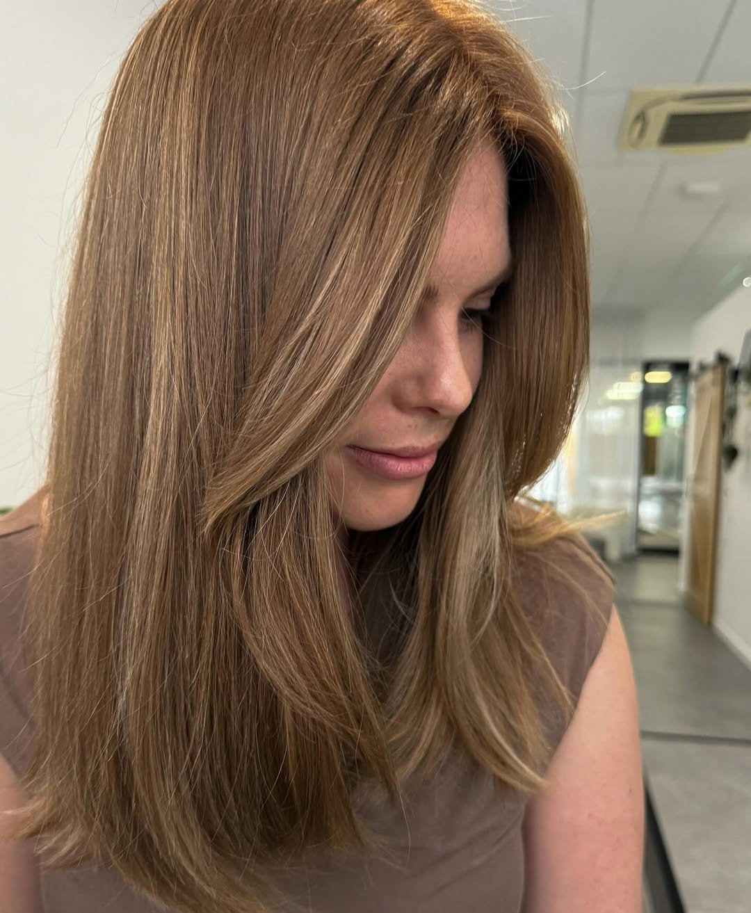 Close-up of a woman with natural, sun-kissed soft summer hair ideas, wearing a light-colored linen top, gazing thoughtfully.