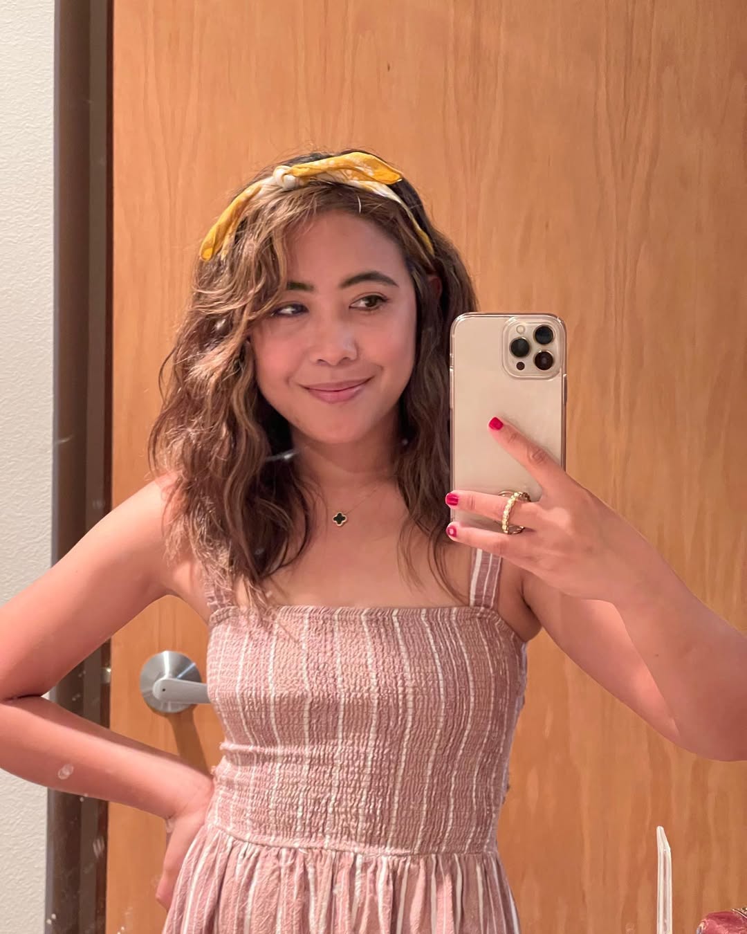 Woman with long, wavy blonde hair styled in a half-up messy bun, perfect for summer beach hair ideas 2026. The look is effortless and chic, ideal for a day by the ocean.