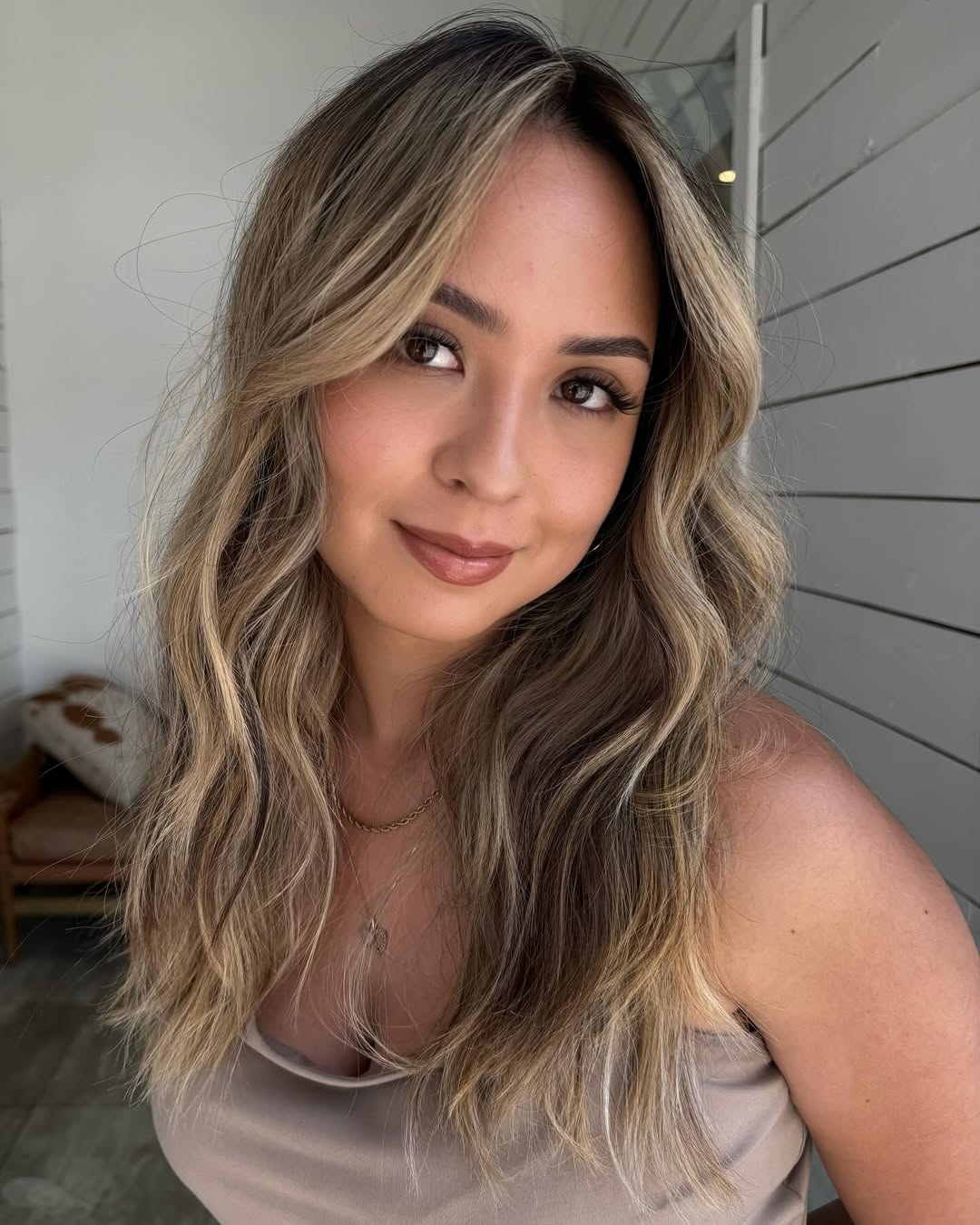 Close-up of a woman with long, sun-kissed blonde hair styled in soft, natural waves, perfect for summer beach hair ideas 2026. She's wearing a casual white top, gazing towards the ocean.