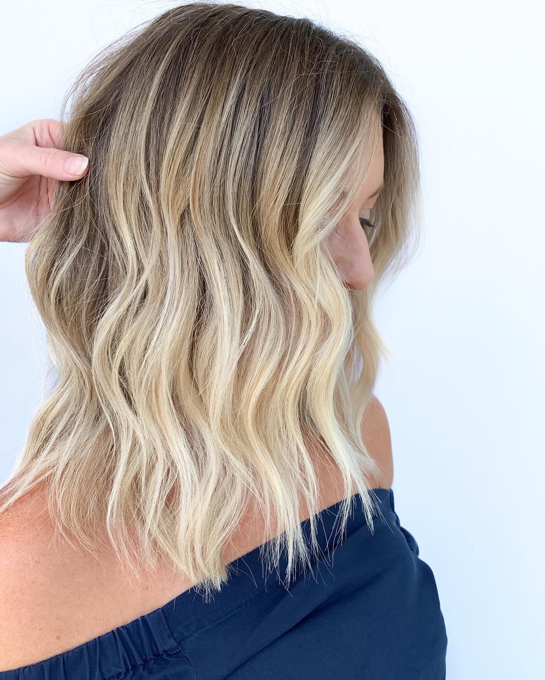 Close-up of a woman with long, sun-kissed blonde hair styled in loose, natural waves, perfect for summer beach hair ideas 2026. She wears a white top, subtly showcasing a casual, effortless vibe.