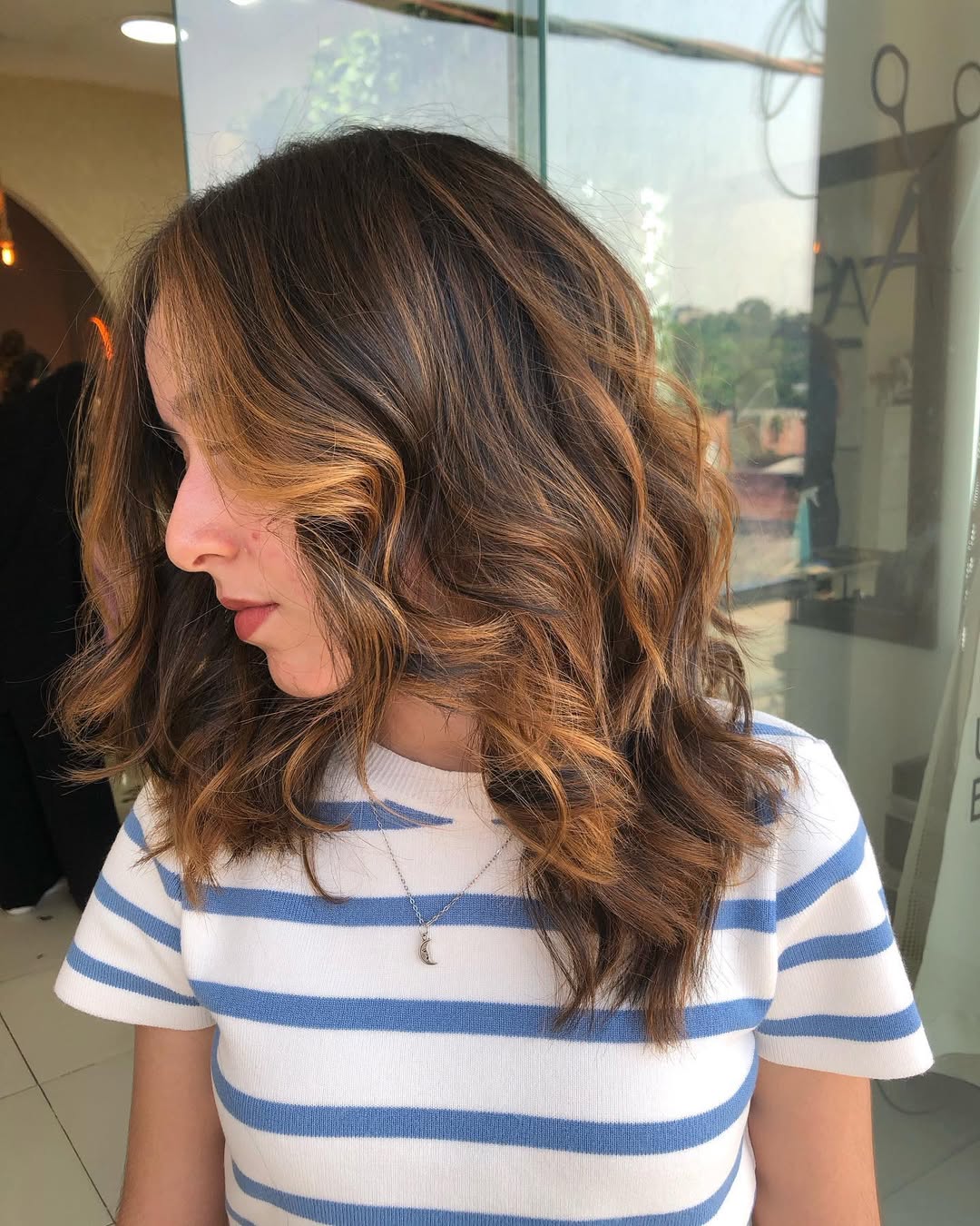 Close-up of a woman with long, textured wavy hair, styled with a subtle side part, perfect for summer beach hair ideas 2026. The natural, effortless look complements a sunny day.