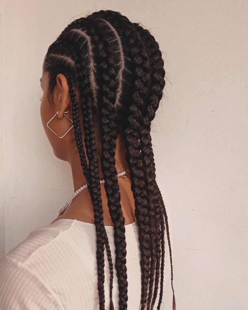 Close-up of a diverse woman with intricate summer braids ideas, showcasing several small cornrows styled into a chic updo for a casual daytime look.
