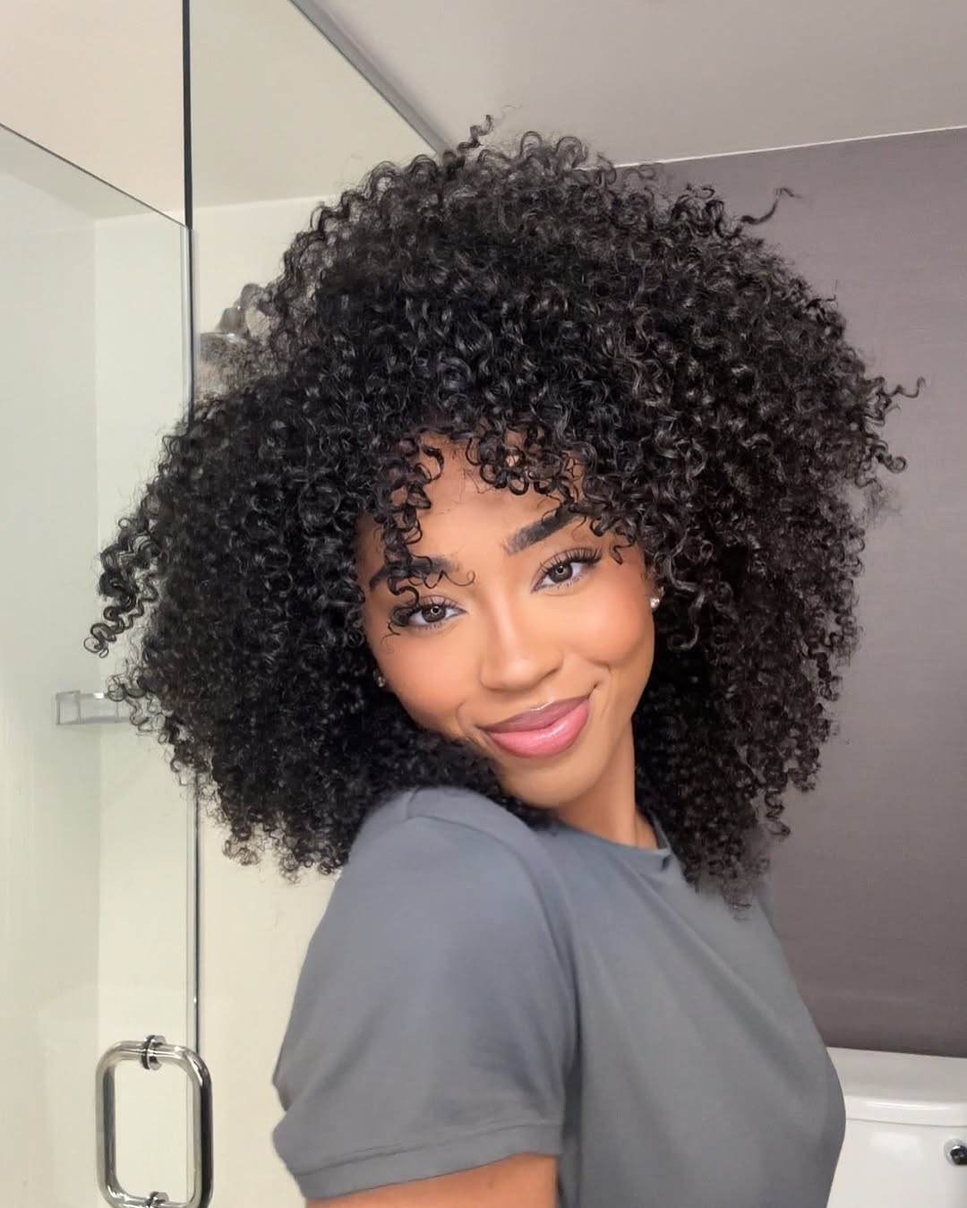 Beautiful woman with voluminous, bouncy summer curly hairstyles 2026, featuring golden-brown loose curls cascading over her shoulders, perfect for a casual sunny day look.