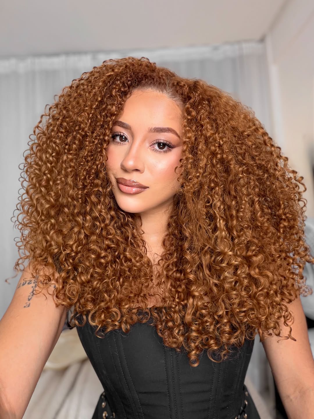 A woman confidently sports vibrant red curly hair styled in a chic, voluminous bob, perfect for summer curly hairstyles 2026. Her elegant black top highlights the striking color and playful bounce of her curls.