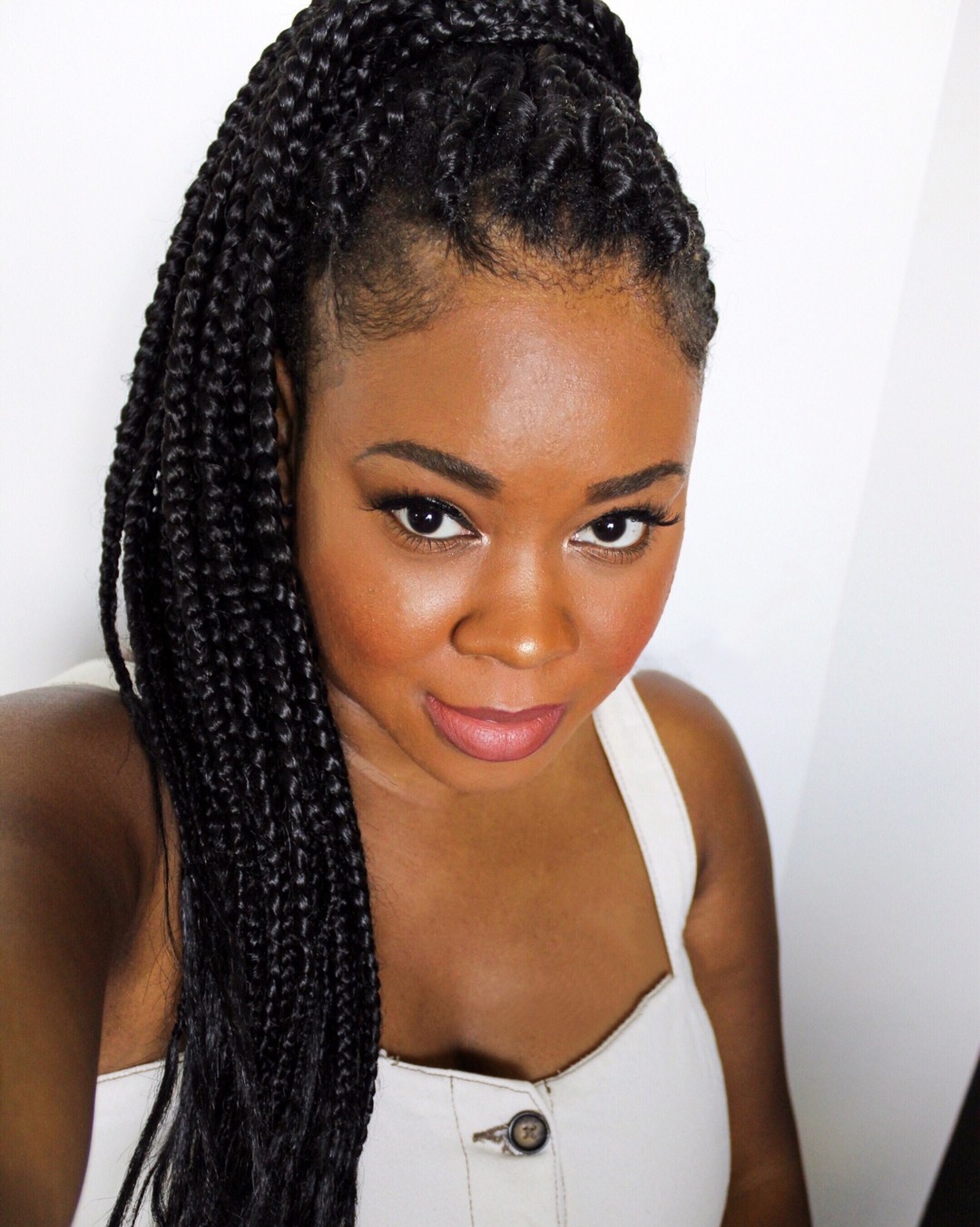 Beautiful black woman wearing a chic, high puff hairstyle with curly ends, perfect for summer. Accessorized with large hoop earrings and a minimal top.