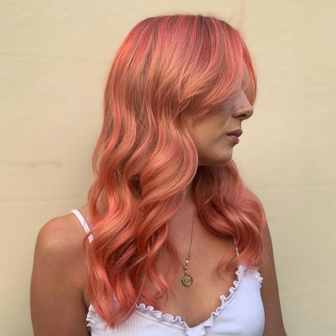 A woman with vibrant true summer hair color 2026, featuring sun-kissed blonde highlights and a rose gold undertone, flowing over a breezy white linen dress for a beach vacation.